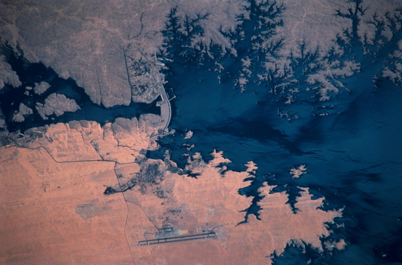 STS102-303-017 (8-21 March 2001)--- The STS-102 crew members used a 35mm camera on the flight deck of the Space Shuttle Discovery to record this image of  the Aswan High Dam.  The structure was completed in 1970 and is one of the largest earthen embankment dams in the world.  It is 364 feet (111 meters) tall, 12,565 feet (3,830 meters) long and nearly 3,281 feet (1,000 meters) wide.  When it was built the new reservoir required relocation of nearly 100,000 residents and some archaeological sites.  Although the reservoir has benefited Egypt by providing power and controlling floods, according to NASA scientists, it has also had detrimental effects on the Nile system.  Before the dam, an estimated 110 million tons of silt was deposited by the annual flood of the Nile, enriching agricultural lands and maintaining the land of the Nile delta.  Now this sediment is trapped behind the dam, requiring artificial fertilization of agricultural lands and leading to erosion and saltwater intrusion where the Nile river meets the Mediterranean Sea.