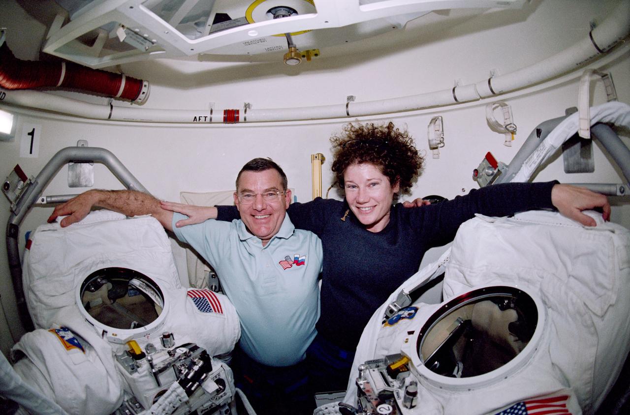 STS102-321-013 (8-21 March 2001) --- Sandwiched between the extravehicular mobility unit (EMU) space suits, astronauts James S. Voss (left) and Susan J. Helms, both Expedition Two flight engineers, are photographed in the shuttle airlock of the Earth-orbiting Space Shuttle Discovery.  Voss and Helms were involved in the first of two space walks performed on the STS-102 mission while docked with the International Space Station (ISS).