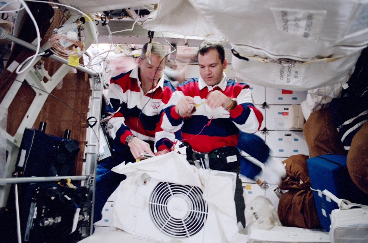 STS102-324-004 (8-21 March 2001) --- Onboard the mid deck of the Earth-orbiting Space Shuttle Discovery, astronauts James D. Wetherbee, STS-102 commander (left) and Paul W. Richards, mission specialist, are photographed performing in-flight maintenance on the cabin fan.