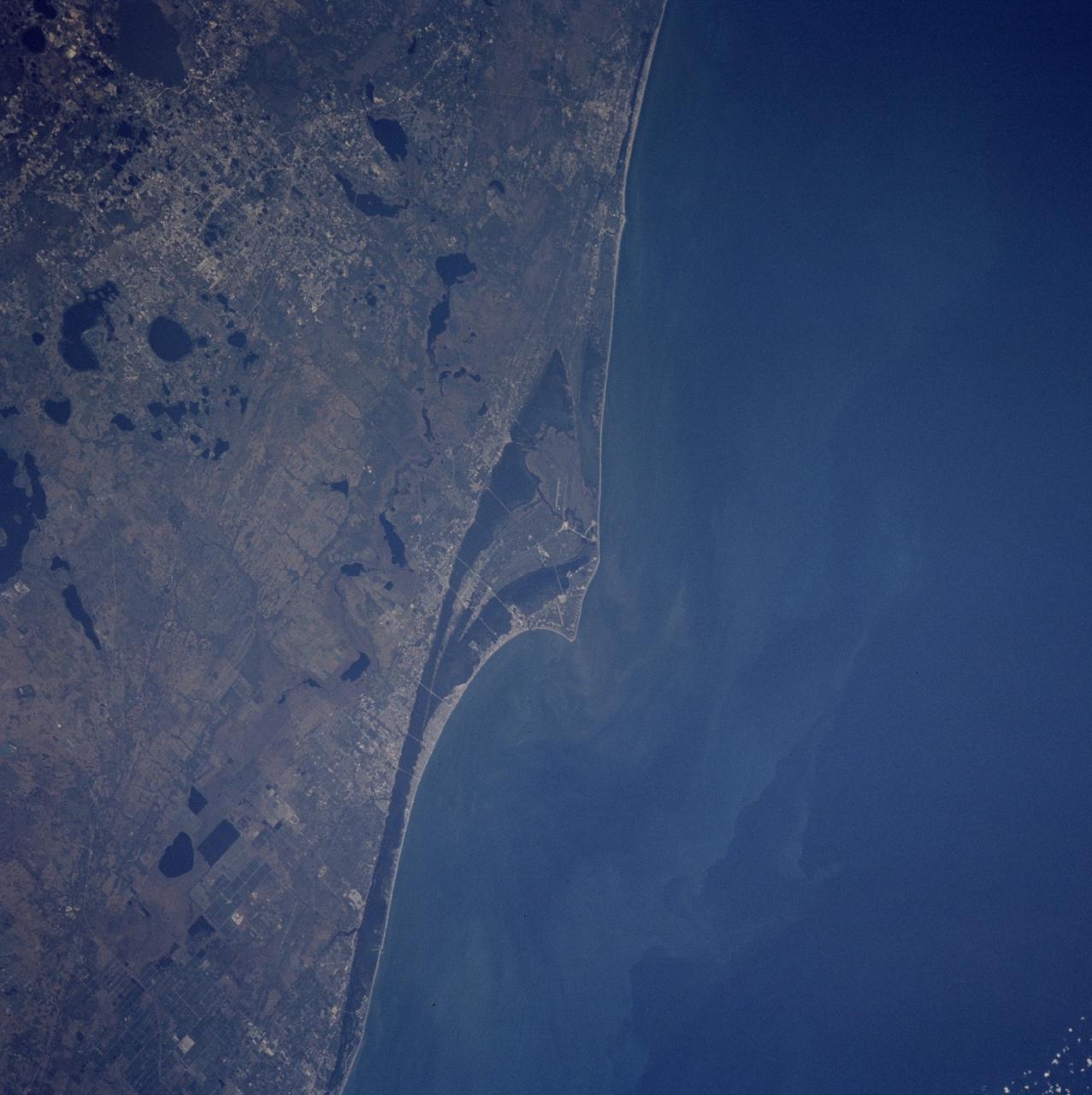 STS103-728-035 (19-27 December 1999) --- One of the astronauts aboard the Earth-orbiting Space Shuttle Discovery used a handheld 70mm camera to photograph this scene of the Kennedy Space Center, Florida and its environs. The old launch pads dot the "V" shaped land (Cape Canaveral) along the coast. On Merritt Island the Shuttle launch pads and runway are visible. The large city surrounded by circular lakes to the west of Cape Canaveral is Orlando.