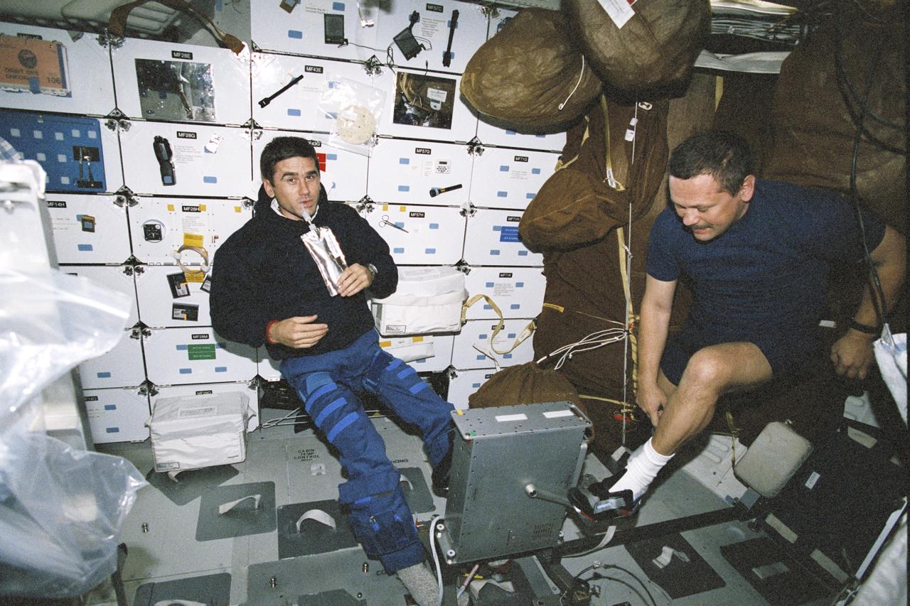 STS106-316-031 (8-20 September 2000) --- Cosmonaut Yuri I. Malenchenko (left), drinks a beverage, as cosmonaut Boris V. Morukov, prepares to exercise using an ergometer on the mid deck of the Space Shuttle Atlantis. Malenchenko and Morukov are mission specialists who represent Rosaviakosmos.