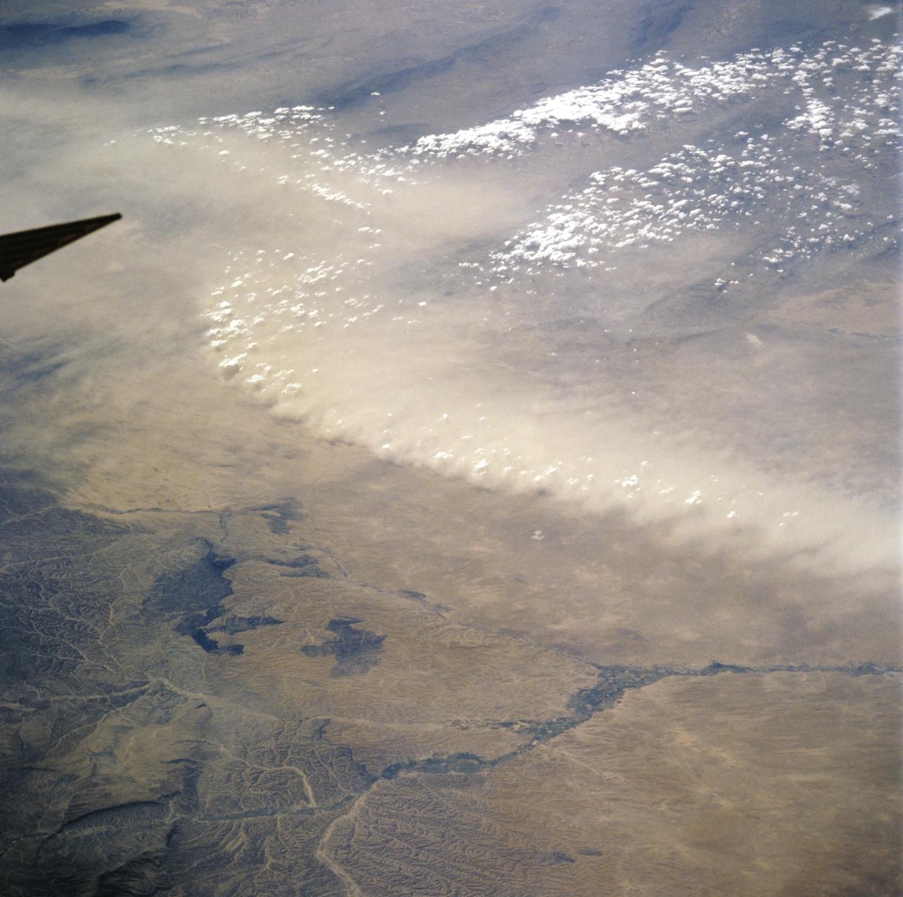 STS106-718-056 (11 September 2000)  --- One of the STS-106 crew members on board the Space Shuttle Atlantis used a handheld 70mm camera to photograph this image of  Afghanistan dust/front winds in the upper Amu Darya Valley. The strong winds along the northern border of Afghanistan lofted thick, light brown dust into the air (top half of the view). In this desert environment land surfaces are not protected by vegetation from the effect of blowing wind. The central Asian deserts experience the greatest number of dust storm days on the planet each year. The sharp dust front shows that the dust has not traveled far, but has been raised from the surfaces in the view. Dust is entrained in the atmosphere by horizontal winds but also by vertical movements. Here the vertical component is indicated by the fact that the higher points along the dust front are each topped by a small cumulus cloud, which appear as a line of small white puffballs. Cumulus clouds indicate upward motion and here the air which has entrained the dust is lifting the air above to the level of condensation at each point where a small cloud has formed.