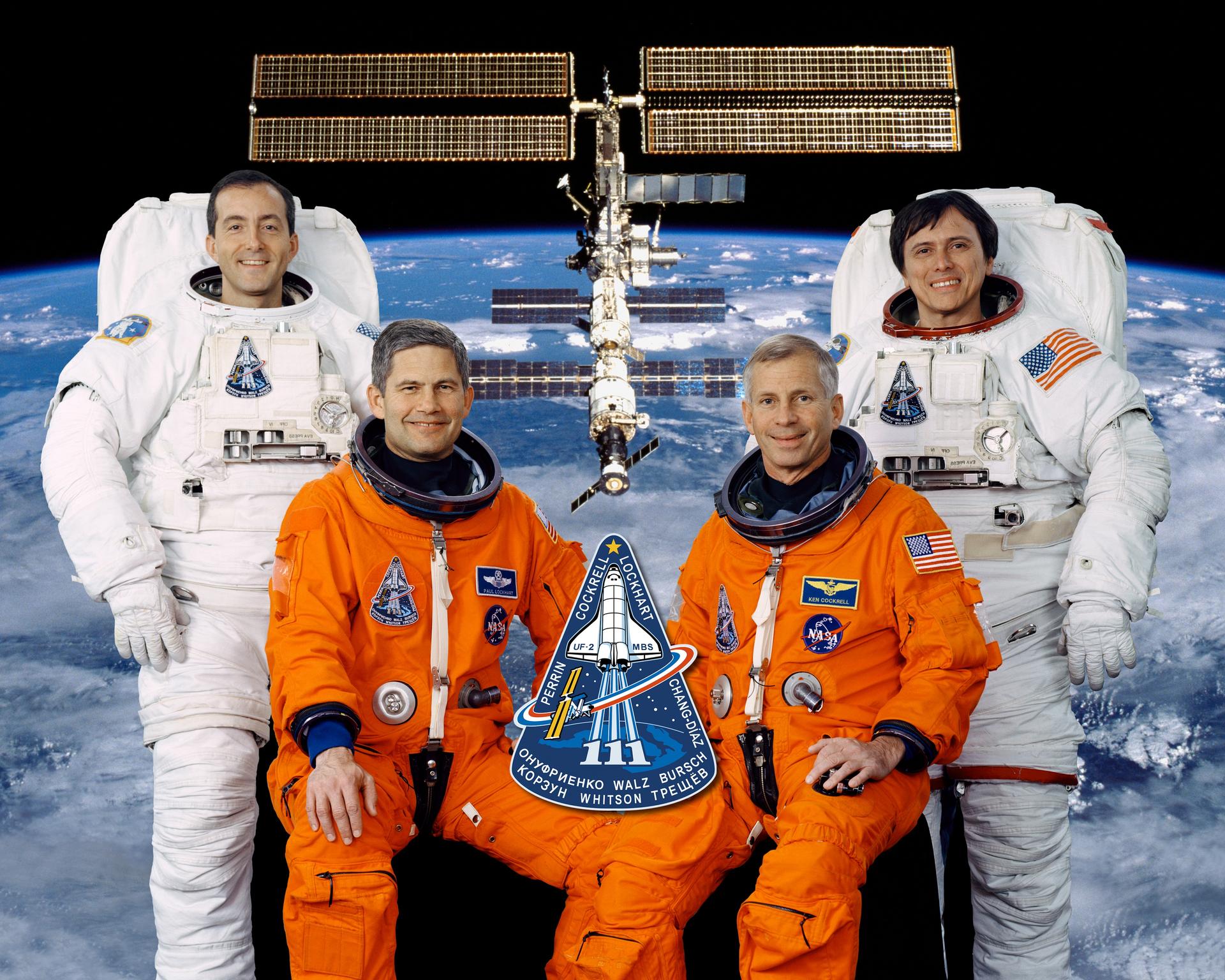 Four crew members pose for portrait in orange and white spacesuits.