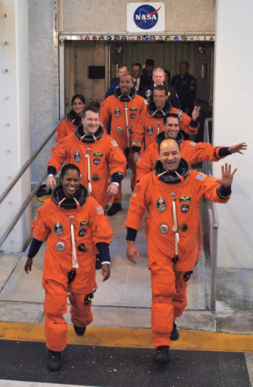 STS116-S-005 (9 Dec. 2006) --- After suiting up, the STS-116 crewmembers exit the Operations and Checkout Building to board the Astrovan, which will take them to launch pad 39B at Kennedy Space Center. On the right (front to back) are astronauts Mark L. Polansky, commander; William S. (Bill) Oefelein, pilot; and Christer Fuglesang, mission specialists representing the European Space Agency (ESA). On the left (front to back) are astronauts Joan E. Higginbotham, Nicholas J. M. Patrick, Sunita L. Williams and Robert L. Curbeam, Jr., all mission specialists. Discovery's seven-member crew will link up with the International Space Station on Monday, Dec. 11, to begin a complex, week-long stay that will rewire the outpost and increase its power supply. During three spacewalks and intricate choreography with ground controllers, the astronauts will bring electrical power on line generated by a giant solar array wing delivered to the station in September.