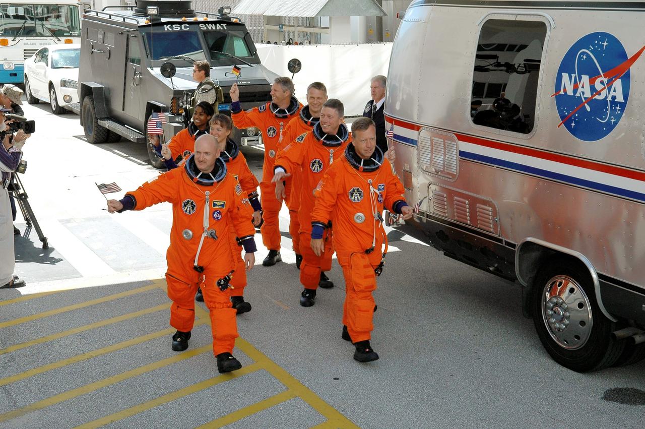 STS121-S-006 (4 July 2006) --- The STS-121 crewmembers, having donned their shuttle launch and entry suits, wave flags for the Fourth of July as they prepare to board the transfer van awaiting to take them to Launch Pad 39B. Steven W. Lindsey (right front), commander, and Mark E. Kelly, pilot, lead the way. Other crewmembers - Lisa M. Nowak, Michael E. Fossum, Stephanie D. Wilson, Piers J. Sellers and European Space Agency (ESA) astronaut Thomas Reiter of Germany - follow.