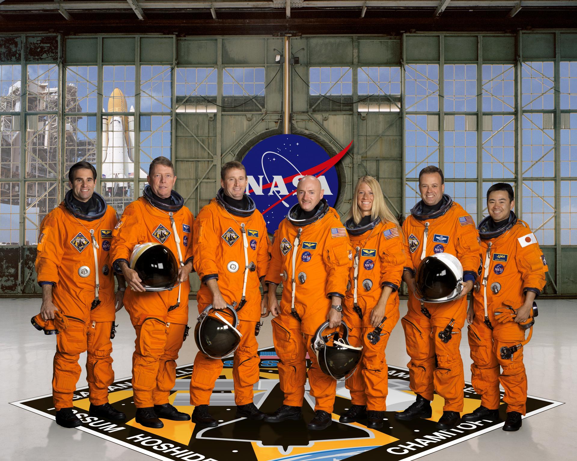 STS-124 crew portrait with the crew standing in the orange launch and entry suits, holding helmets, in from of the NASA meatball patch.