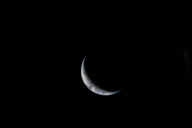 A sliver of Earth is illuminated against the blackness of...