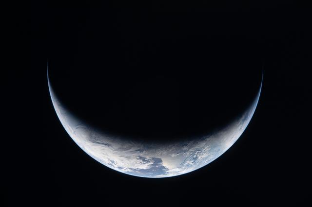 A sliver of Earth is illuminated against the blackness of space in this photo...
