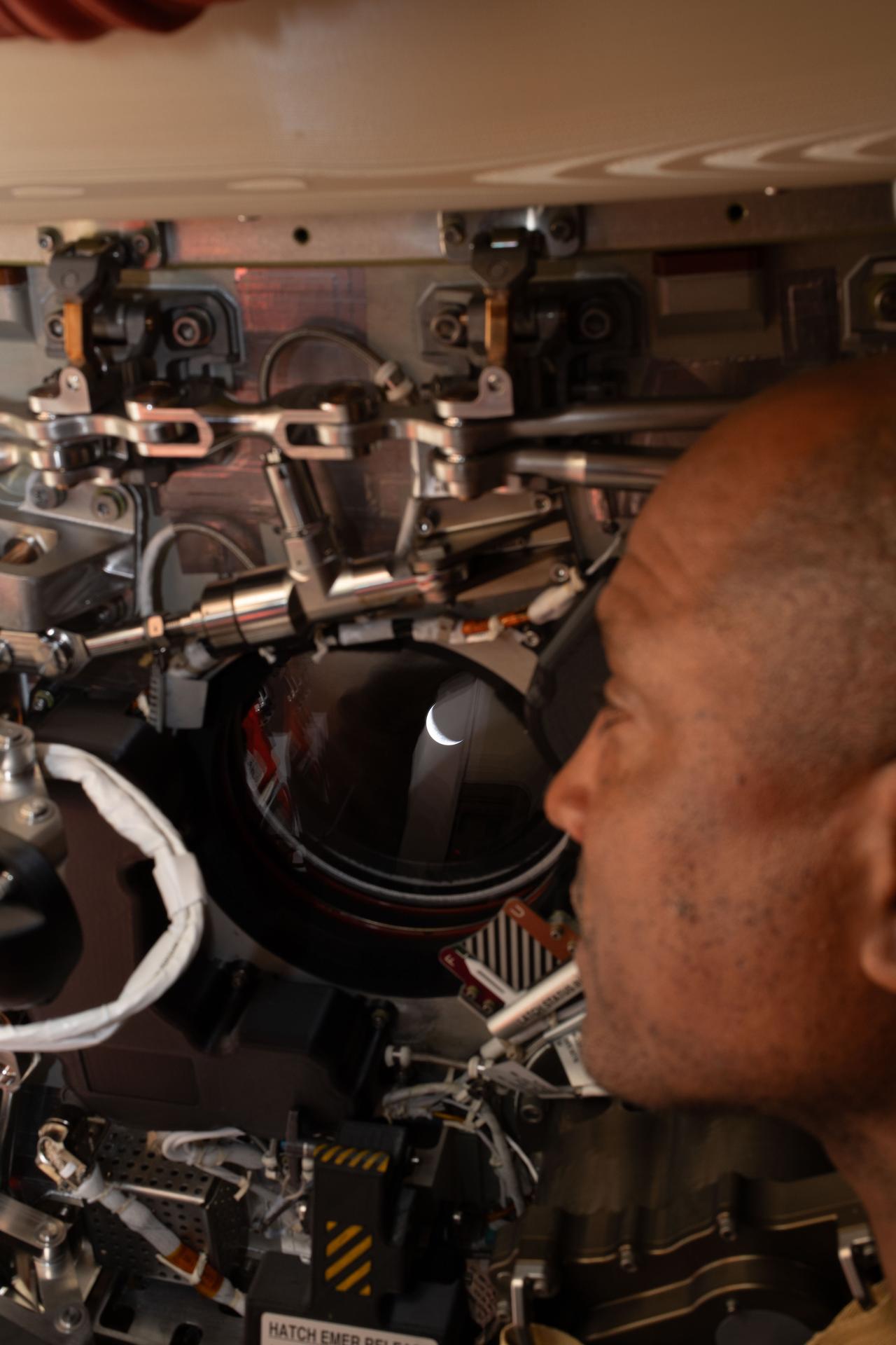 art002e009273 (April 6, 2026) - Artemis II pilot and NASA astronaut Victor Glover peers out one of the Orion spacecraft's...