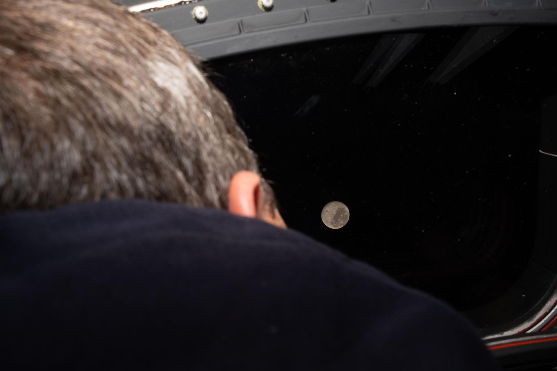 art002e024097 (April 5, 2026) - NASA astronaut and Artemis II commander Reid Wiseman peers out the window of the Orion spacecraft at the near side of the Moon before going to sleep on Flight Day 5, the night before lunar flyby. Orion and the Artemis II crew aboard entered the lunar sphere of influence at 12:37 a.m. ET on April 6, at the tail end of the fifth day of their mission. Credit: NASA