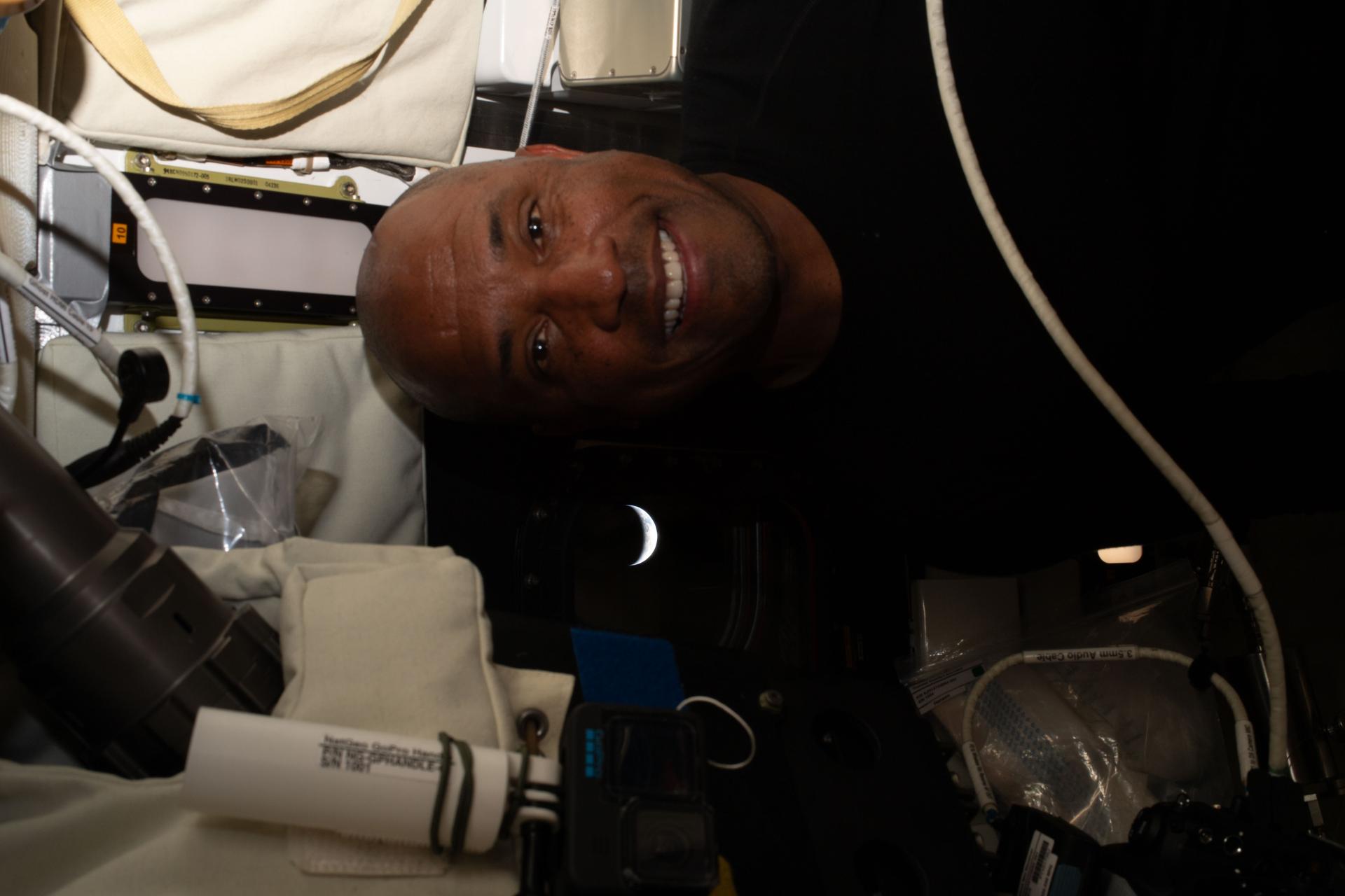 art002e025219 (April 9, 2026) - NASA astronaut Victor Glover pictured inside the Orion spacecraft with the crescent Earth pictured through the window behind him. This picture was captured after the Artemis II crew completed their lunar flyby and were on their way back to Earth. Credit: NASA