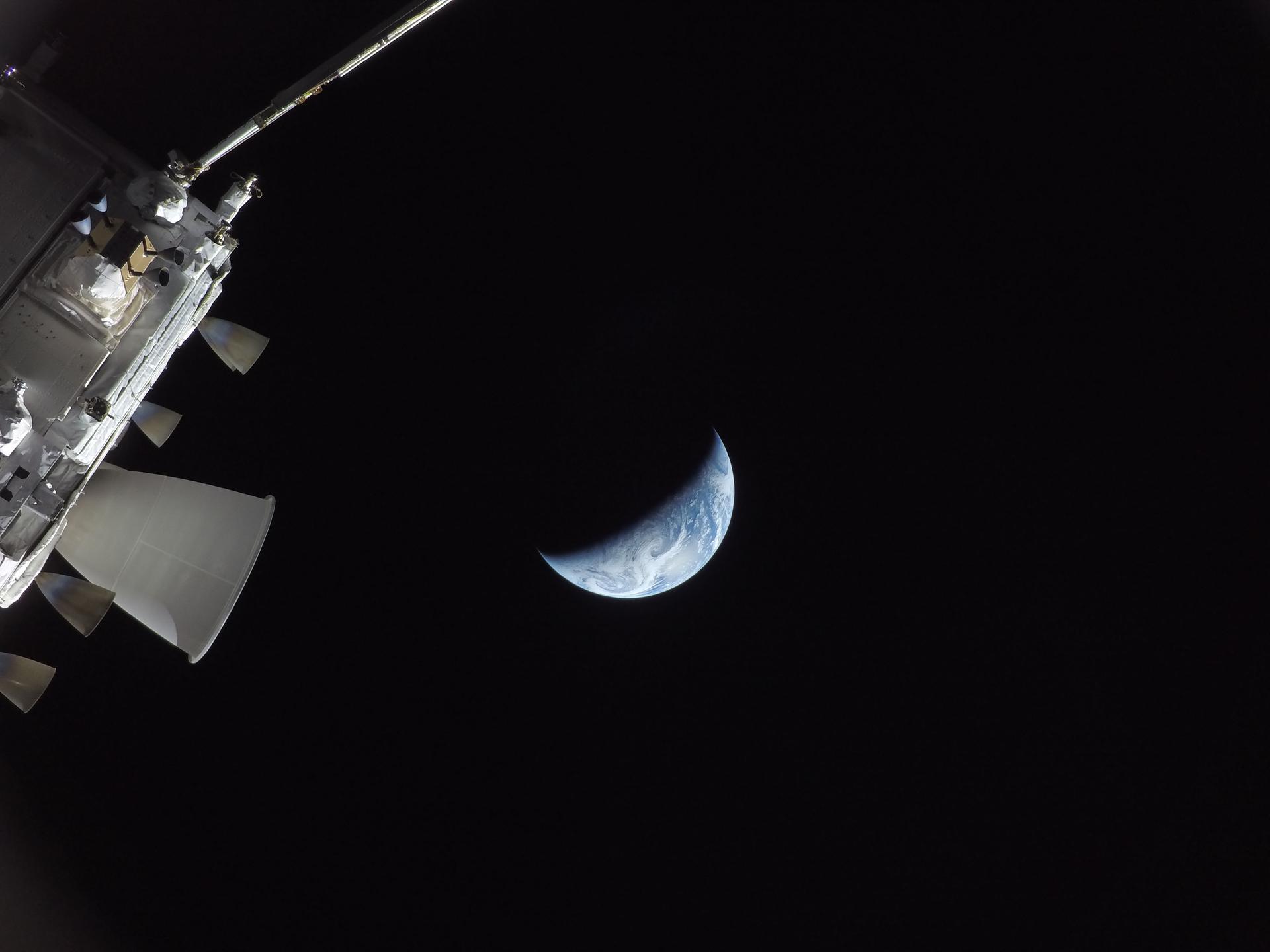 art002e031476 (April 10, 2026) - During the Artemis II crew’s journey back home to Earth, NASA’s Orion spacecraft appears alongside a sliver of Earth, both illuminated against the blackness of space. Pictured from one of the cameras mounted on Orion’s solar array wings, this image shows the orbital maneuvering system engine, five of eight auxiliary thrusters, and a pod of four reaction control system thrusters on the spacecraft’s service module. Credit: NASA