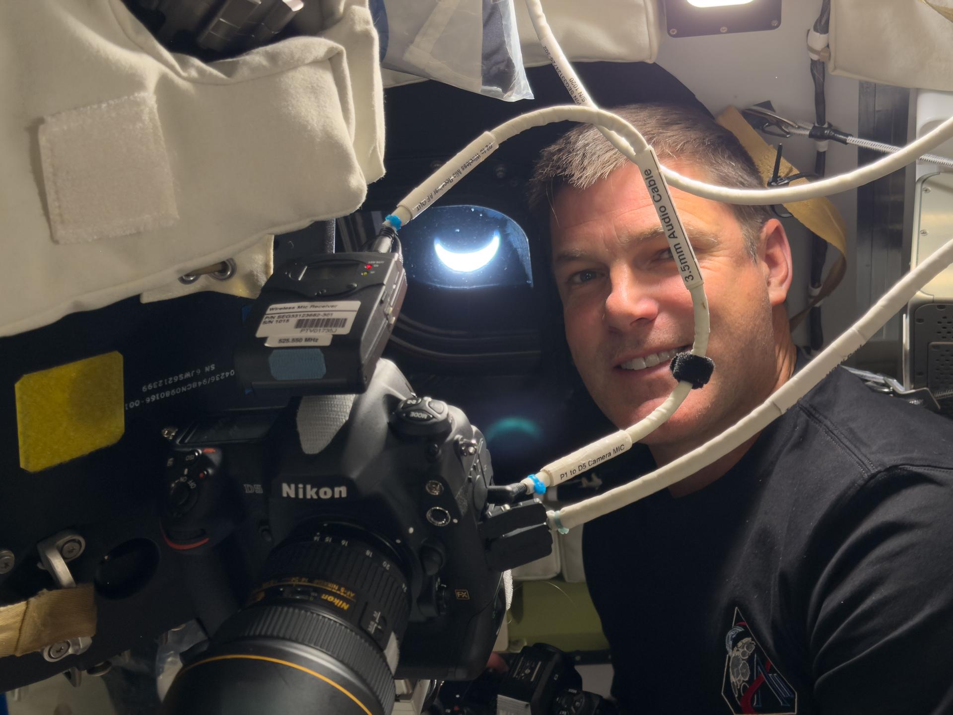 art002e041703 (April 8, 2026) – CSA astronaut Jeremy Hansen pictured inside the Orion spacecraft with the crescent Earth pictured through the window behind him. This picture was captured after the Artemis II crew completed their lunar flyby and were on their way back to Earth. Credit: NASA