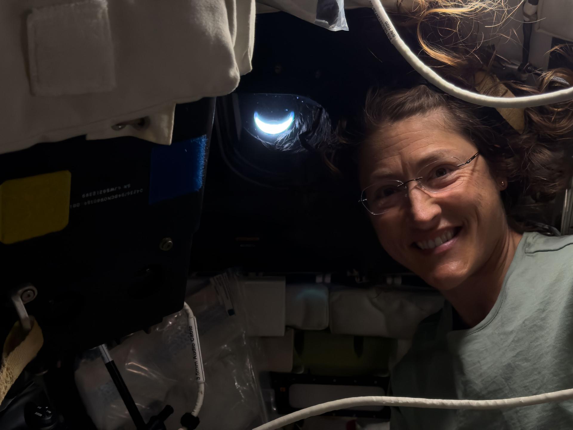 art002e041711 (April 8, 2026) - NASA astronaut Christina Koch pictured inside the Orion spacecraft with the crescent Earth pictured through the window behind her. This picture was captured after the Artemis II crew completed their lunar flyby and were on their way back to Earth. Credit: NASA