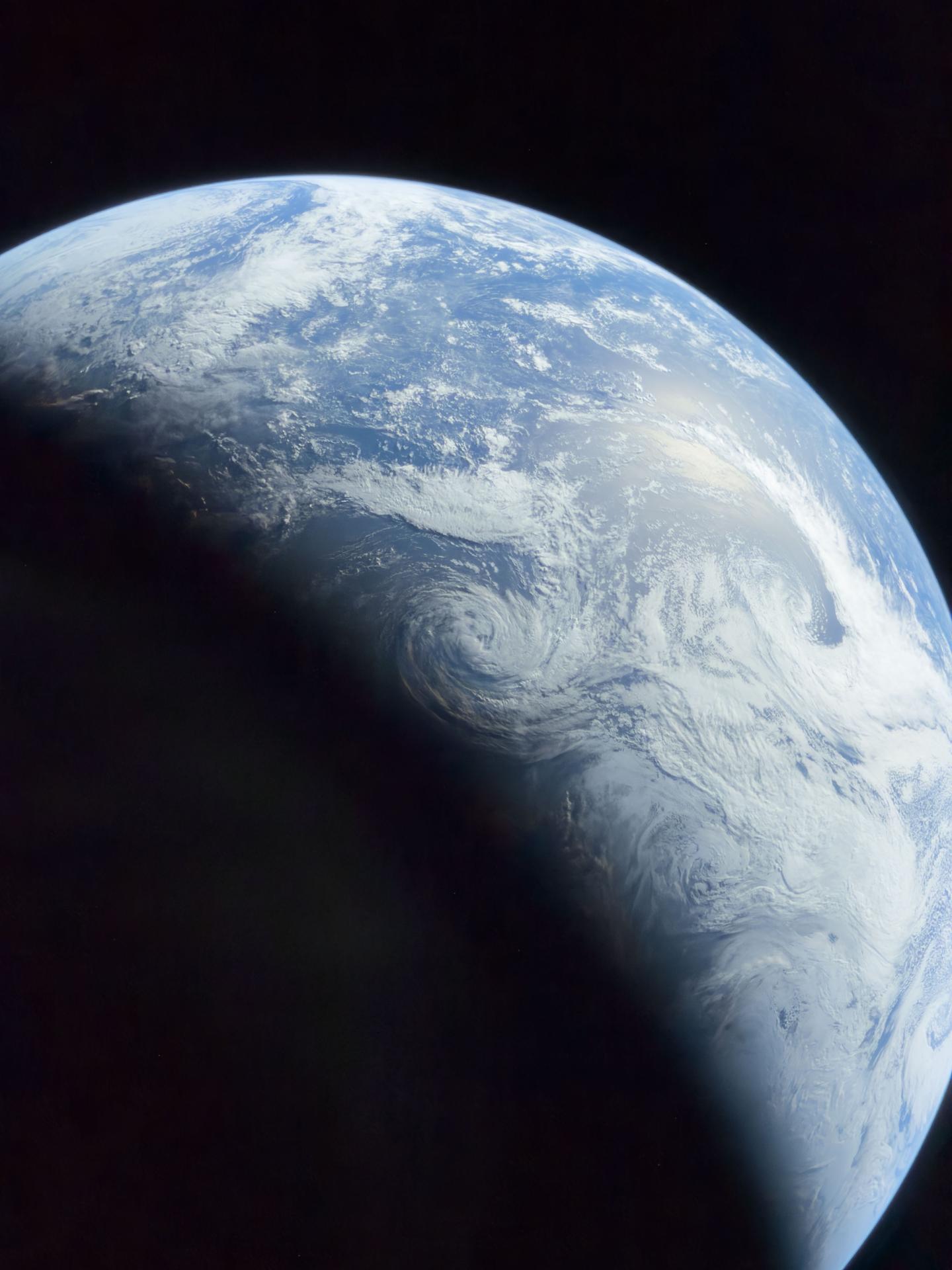 art002e042281 (April 10, 2026) - Earth captured from the Artemis II crew showing white swirling clouds above the blue Pacific Ocean, with reflected sunlight visible in the upper right and the lower left obscured in darkness behind the terminator. This image was captured a few hours before the crew returned to Earth. Credit: NASA