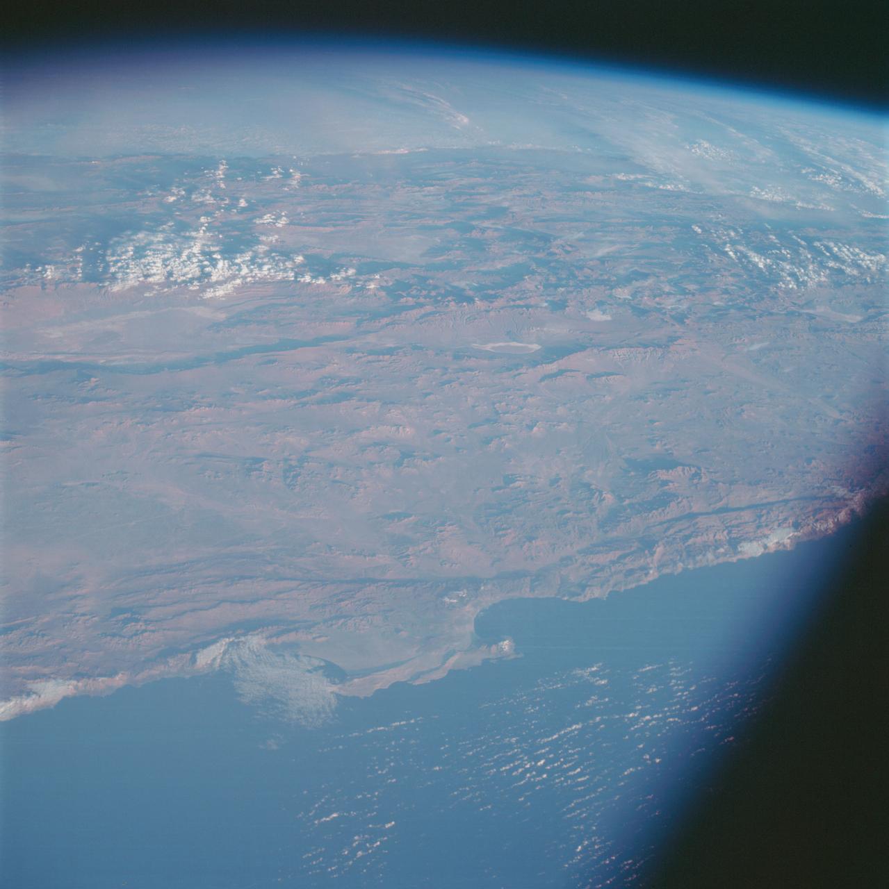 AS07-07-1826 (17 Oct. 1968) --- This view of South America was photographed from the Apollo 7 spacecraft during its 81st revolution of Earth from an altitude of 120 nautical miles. The port city of Antofagasta, Chile, is located in the half-moon shaped bay in the lower left portion of the picture. Beyond the coast is the Andean peak of Llullaillaco Volcano which rises 22,000 feet above sea level. At left center is the Chuquicamata copper mines located near Coloma. At the center of the photo, behind the large salt lake and atop a 19,000 foot high volcano, the countries of Bolivia, Argentina, and Chile meet at a common point. Below the clouds in the upper portion of the photo are the Great Plains known as the Gran Chaco.