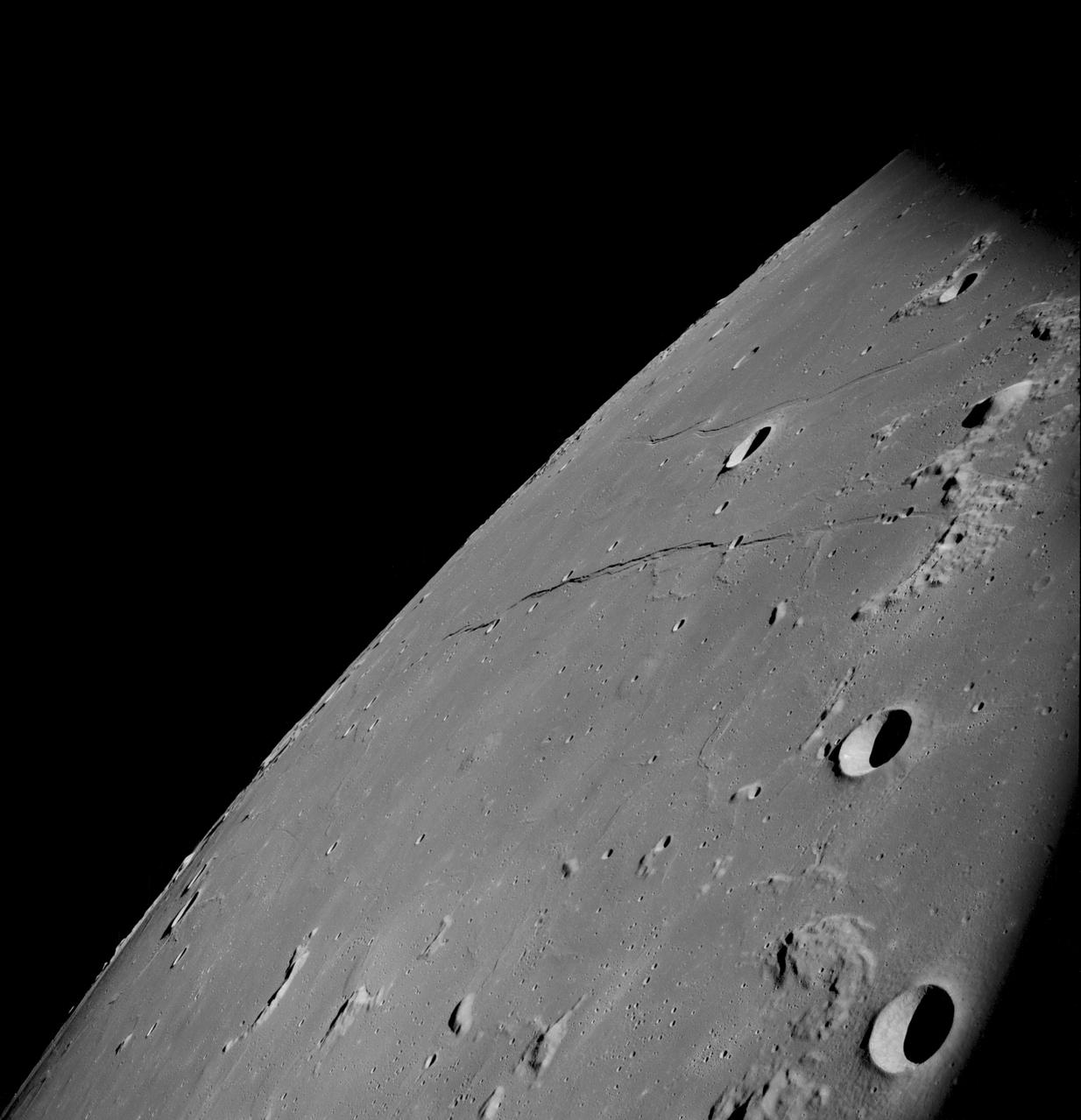 AS08-13-2344 (21-27 Dec. 1968) --- This oblique photograph looks generally northwest from the Apollo 8 spacecraft into the Sea of Tranquility. (HOLD PICTURE WITH LARGE TRIANGLE FORMED BY DARK SKY AT UPPER LEFT). The three prominent craters are Taruntius F in the lower right corner; Taruntius E in the center; and Cauchy between the two linear features. The Cauchy scarp, this side of the Cauchy crater, is formed by one to three faults stepped down toward the spacecraft. Cauchy Rille, on the other side of Cauchy crater, consists of several arcuate segments of a graben. Each of the three prominent craters is 10 to 15 kilometers (6 to 9 statute miles) across.