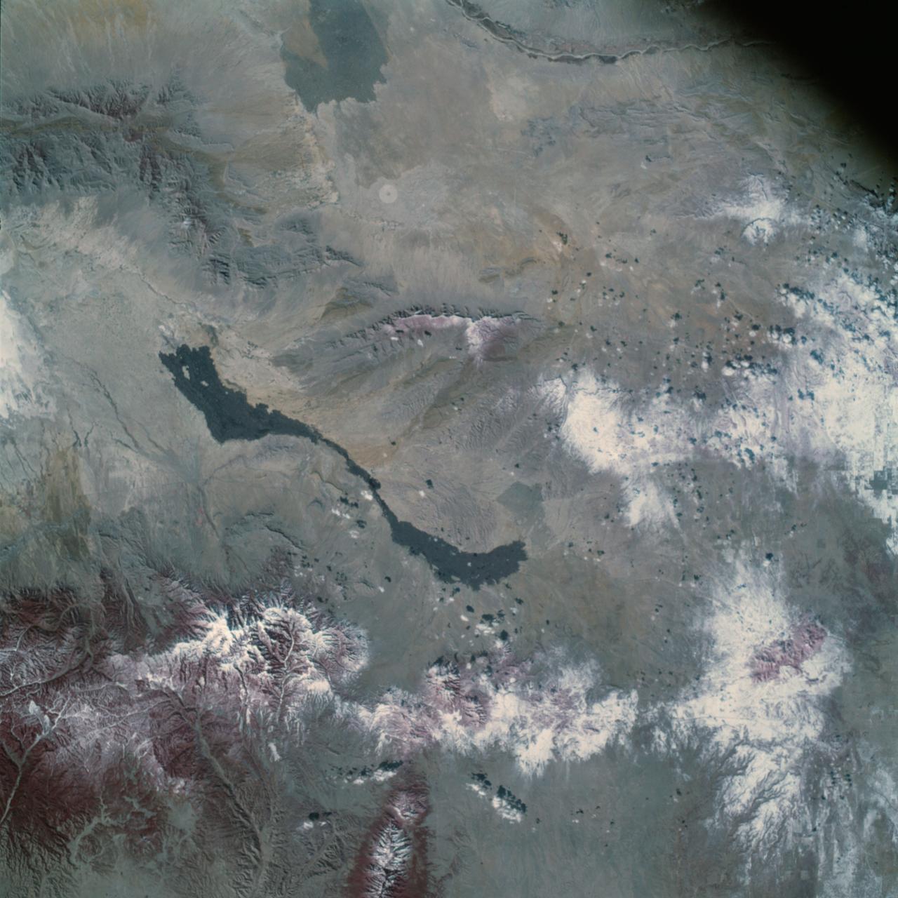 Earth Observation taken by the Apollo 9 crew. View is of Carrizozo in New Mexico and includes lava flow and snow.  Latitude was 33.42 N by Longitude 106.10 W, Overlap was 7.5%, Altitude miles were 121 and cloud cover was 0%.  This imagery taken as part of the NASA S0-65 Experiment  "Multispectral Terrain Photography". The experiment provides simultaneous satellite photography of the Earth's surface in three distinct spectral bands. The photography consists of four almost spatially identical photographs. The images of ground objects appear in the same coordinate positions on all four photos in the multispectral set within the opto-mechanical tolerances of the Hasselblad cameras in the Apollo 9 spacecraft. Band designation for this frame is A.  Film and filter is Ektachrome SO-368,Infrared Color Wratten 15.  Mean Wavelength of Sensitivity is green,red and infrared. The Nominal Bandpass is total sensitivity of all dye layers 510-900nm.