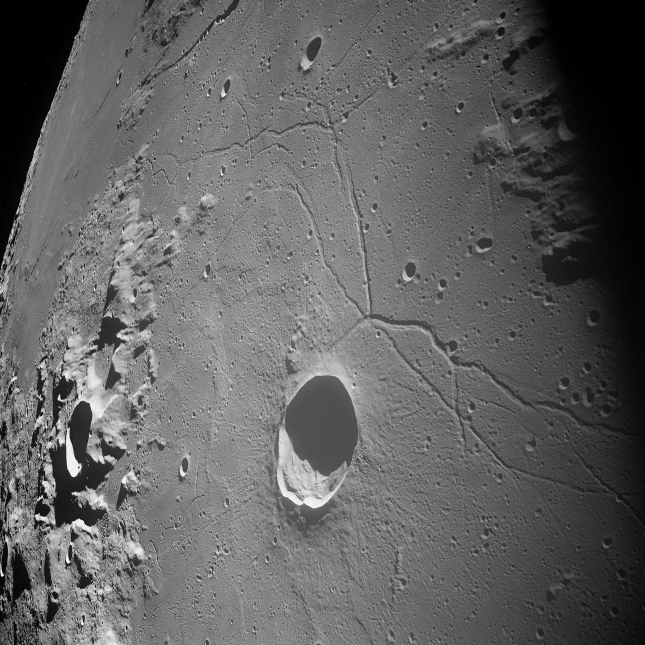 AS10-32-4819 (18-26 May 1969) --- An Apollo 10 northwestward oblique view of Triesnecker crater, centered near 3.6 degrees east longitude, and 4 degrees north latitude. HOLD PICTURE WITH SKY AT UPPER RIGHT. This picture, taken from the Command and Service Modules, shows terrain features typical of northeastern Central Bay. Beyond the highlands, the smooth floor of the Sea of Vapors extends almost to the horizon some 600 kilometers (375 statute miles) from the spacecraft. Triesnecker crater, about 27 kilometers (17 statute miles) in diameter, was 135 kilometers (85 statute miles) northwest of Apollo 10 when the picture was taken. The intersecting linear features to the right of Triesnecker crater are the Triesnecker Rilles.