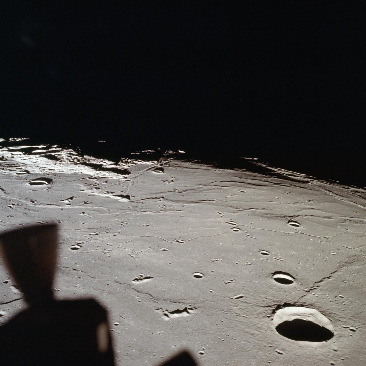 AS11-37-5437 (20 July 1969) --- The approach to Apollo Landing Site 2 in southwestern Sea of Tranquility is seen in this photograph taken from the Apollo 11 Lunar Module (LM) in lunar orbit. When this picture was made, the LM was still docked to the Command and Service Modules (CSM). Site 2 is located just right of center at the edge of the darkness. The crater Maskelyne is the large one at the lower right. Hypatia Rille (U.S. 1) is at upper left, with the crater Moltke just to the right (north) of it. Sidewinder Rille and Diamondback Rille extend from left to right across the center of the picture. This view looks generally west.
