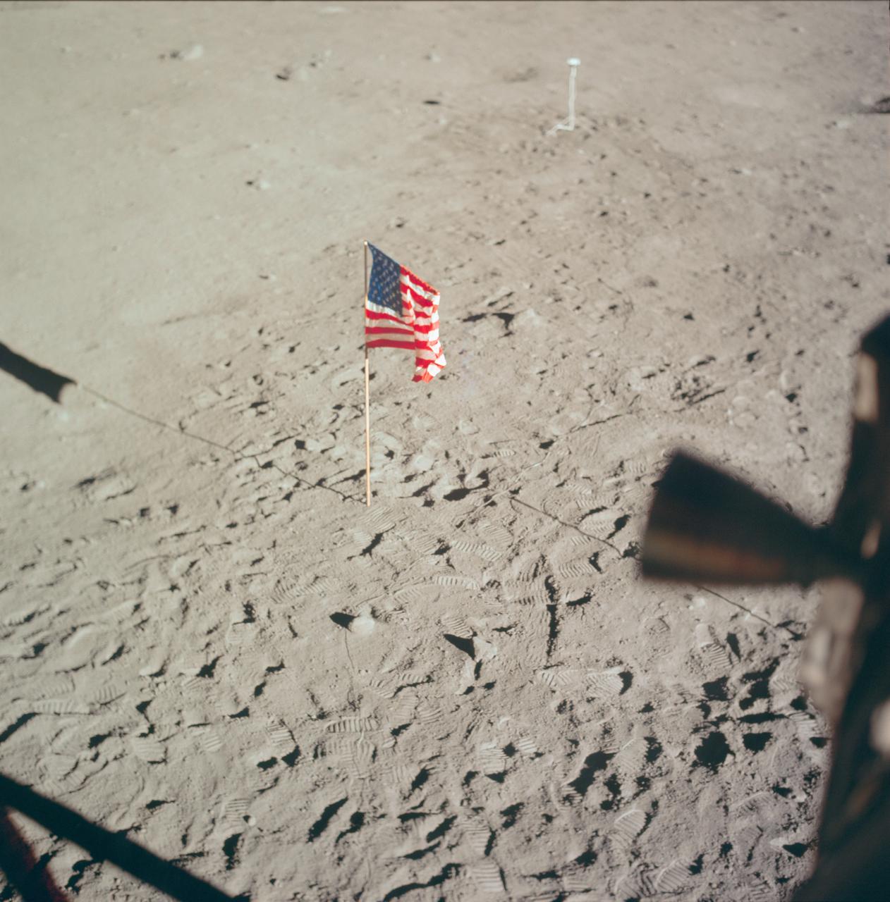 AS11-37-5545 (20 July 1969) --- The flag of the United States, deployed on the surface of the moon, dominates this photograph taken from inside the Lunar Module (LM). The footprints of astronauts Neil A. Armstrong and Edwin E. Aldrin Jr. stand out very clearly. In the far background is the deployed black and white lunar surface television camera which televised the Apollo 11 lunar surface extravehicular activity (EVA). While astronauts Armstrong, commander, and Aldrin, lunar module pilot, descended in the Lunar Module (LM) "Eagle" to explore the Sea of Tranquility region of the moon, astronaut Michael Collins, command module pilot, remained with the Command and Service Modules (CSM) "Columbia" in lunar orbit.