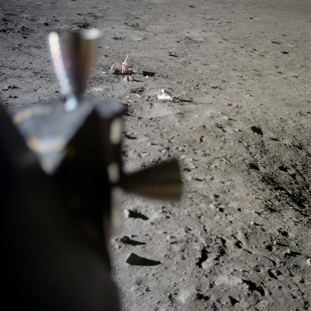 AS11-37-5551 (20 July 1969) --- Two components of the Early Apollo Scientific Experiments Package (EASEP) are seen deployed on the lunar surface in this view photographed from inside the Lunar Module (LM).  In the far background is the Passive Seismic Experiment Package (PSEP); and to the right and closer to the camera is the Laser Ranging Retro-Reflector (LR-3).  The footprints of Apollo 11 astronauts Neil A. Armstrong and Edwin E. Aldrin Jr. are very distinct in the lunar soil.
