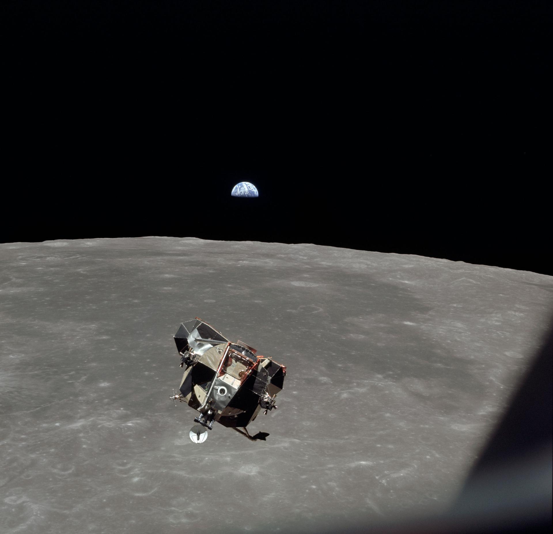 View of the Apollo 11 Lunar Module in lunar orbit as seen by Michael Collins on the command module. The Moon is seen in the background and the Earth can be seen in the distance right over the horizon.