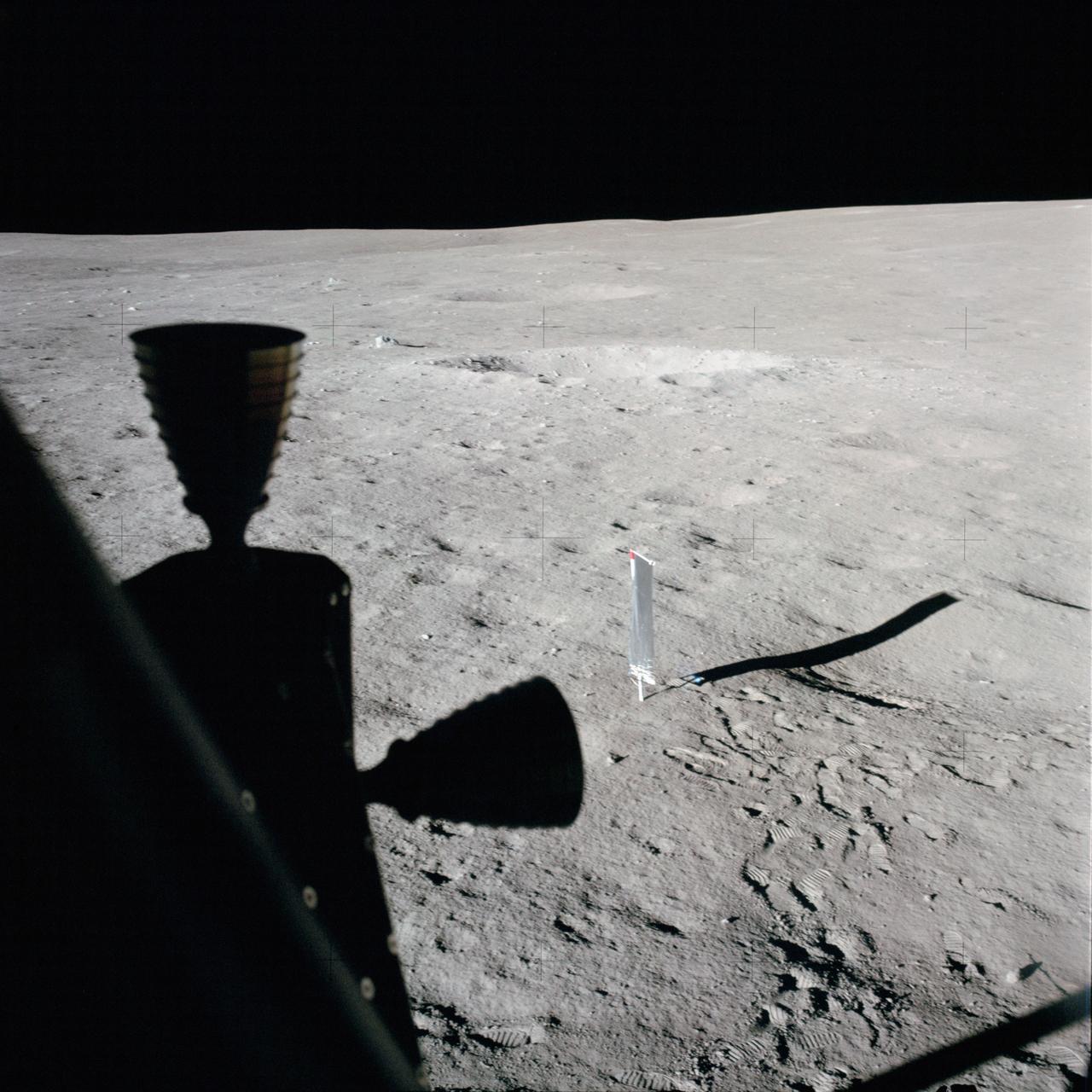 AS14-66-9322 (5-6 Feb. 1971) --- This photograph taken through a window of the Apollo 14 Lunar Module (LM), on the moon, shows an excellent view of the nearby terrain. In the center background is the deployed solar wind composition (SWC) experiment. Two LM RCS thrusters are silhouetted in the left foreground. While astronauts Alan B. Shepard Jr., commander; and Edgar D. Mitchell, lunar module pilot; descended in the LM, astronaut Stuart A. Roosa, command module pilot, remained with the Command and Service Modules (CSM) in lunar orbit.