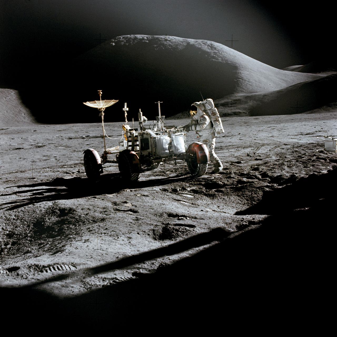 AS15-86-11603 (31 July 1971) --- Astronaut James B. Irwin, lunar module pilot, works at the Lunar Roving Vehicle during the first Apollo 15 lunar surface extravehicular activity (EVA) at the Hadley-Apennine landing site. The shadow of the Lunar Module "Falcon" is in the foreground. This view is looking northeast, with Mount Hadley in the background. This photograph was taken by astronaut David R. Scott, commander.