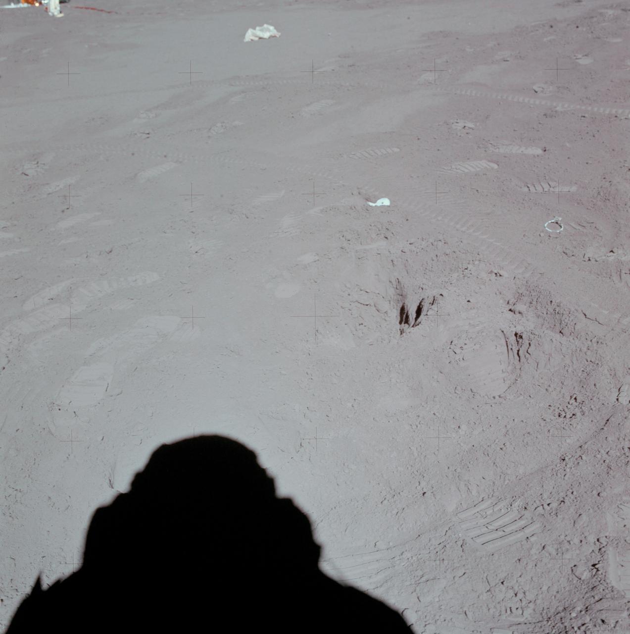 AS15-88-11872 (31 July 1971) --- This north-looking view at Station 8 near the Hadley-Apennine landing site was photographed by one of the missions two moon explorer's (see shadow, foreground) during the third Apollo 15 extravehicular activity (EVA). Prints from the boots of astronauts David R. Scott, commander, and James B. Irwin, lunar module pilot, as well as tire tracks from the Lunar Roving Vehicle (LRV) are scattered throughout the view. A small part of the Apollo Lunar Surface Experiments Package (ALSEP) is in the upper left corner. Lunar samples 15252 and 15253 were removed from this area and returned to Earth for analysis by scientists. While astronauts Scott and Irwin descended in the Lunar Module (LM) "Falcon" to explore the Hadley-Apennine area of the moon, astronaut Alfred M. Worden, command module pilot, remained with the Command and Service Modules (CSM) in lunar orbit.