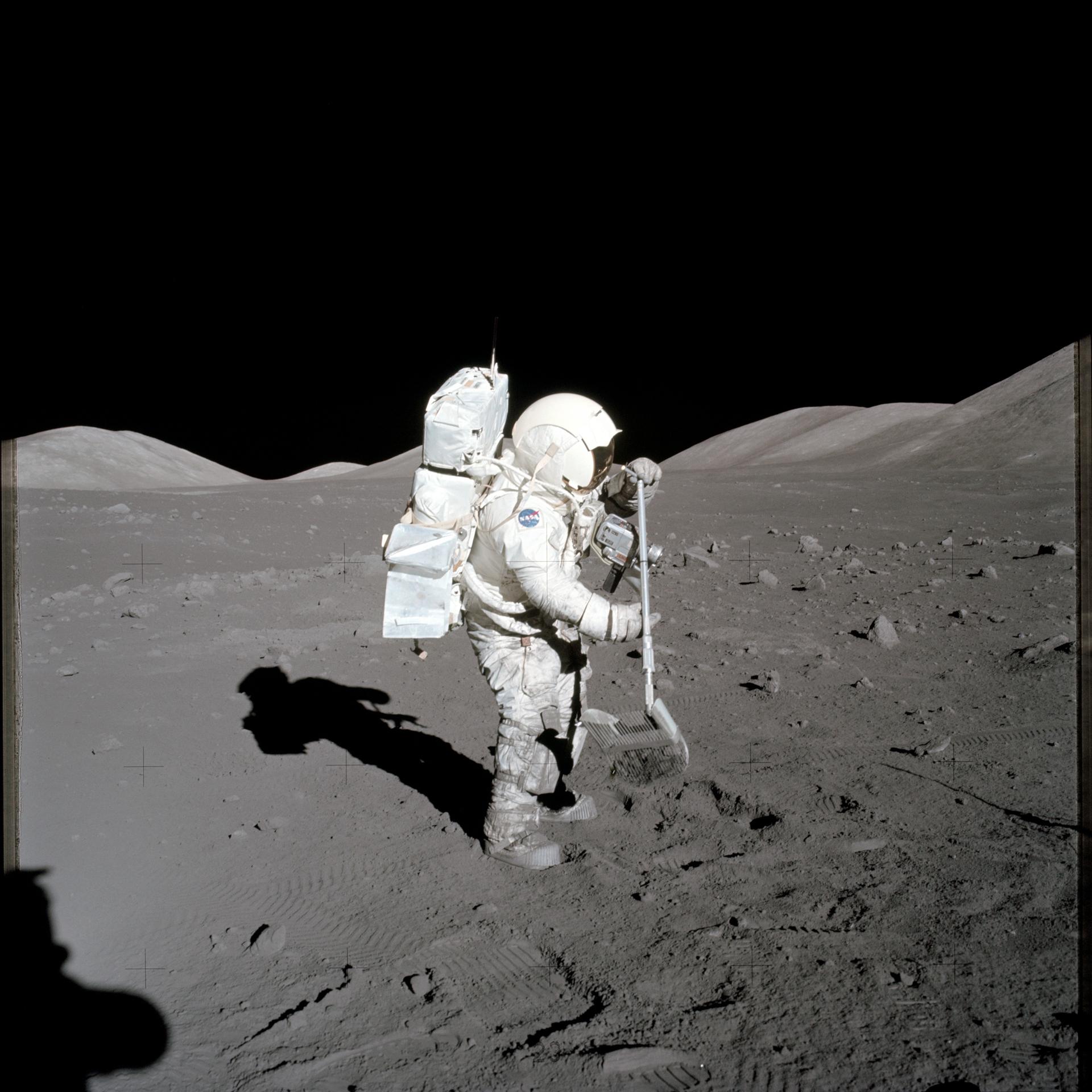 An astronaut in a white spacesuit stands with his shovel poised above the lunar surface.