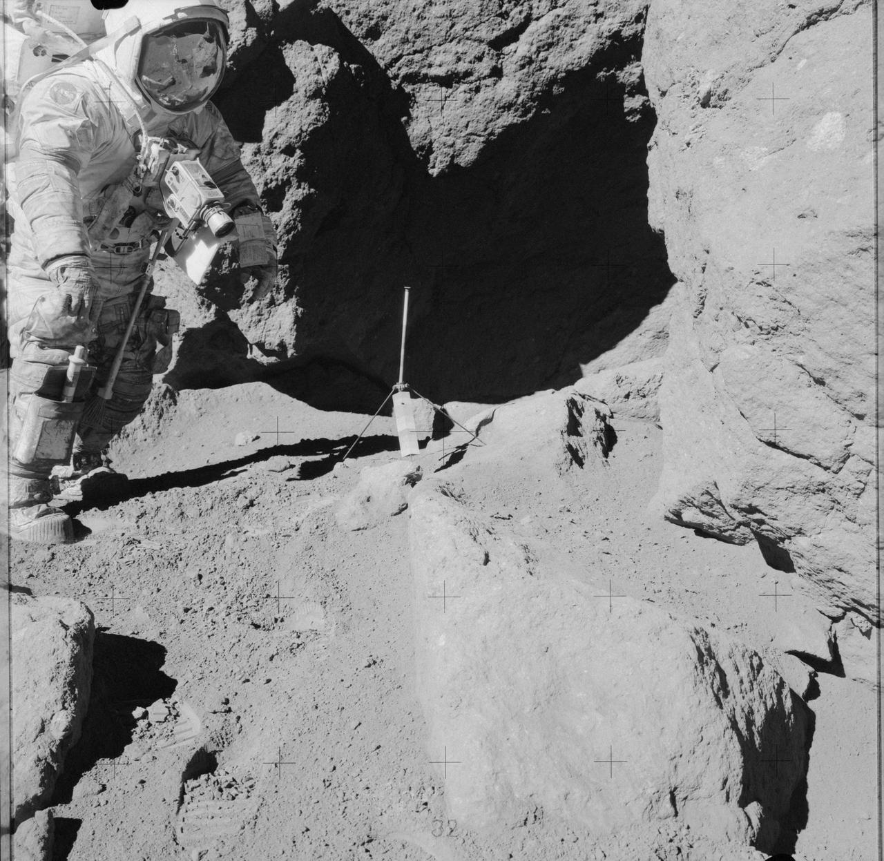 AS17-141-21608 (13 Dec. 1972) --- Astronaut Eugene A. Cernan stands near an over-hanging rock during the third Apollo 17 lunar surface extravehicular activity (EVA) at the Taurus-Littrow landing site. Scientist-astronaut Harrison H. Schmitt took this photograph. The tripod-like object just outside the shaded area is the gnomon and photometric chart assembly which is used as a photographic reference to establish local vertical sun angle, scale and lunar color. The gnomon is one of the Apollo Lunar Geology Hand Tools. While astronauts Cernan and Schmitt descended in the Lunar Module "Challenger" to explore the moon, astronaut Ronald E. Evans remained with the Apollo 17 Command and Service Modules in lunar orbit.