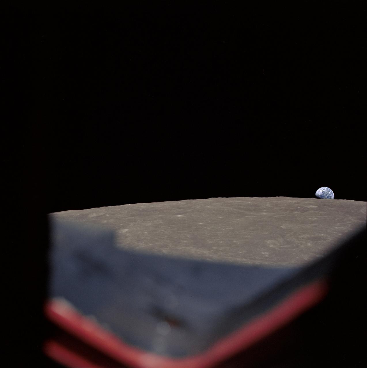 AS8-14-2392 (21-27 Dec. 1968) --- High-oblique view of the moon's surface showing Earth rising above the lunar horizon, looking west-southwest, as photographed from the Apollo 8 spacecraft as it orbited the moon. The center of the picture is located at about 105 degrees east longitude and 13 degrees south latitude. The lunar surface probably has less pronounced color than indicated by this print.