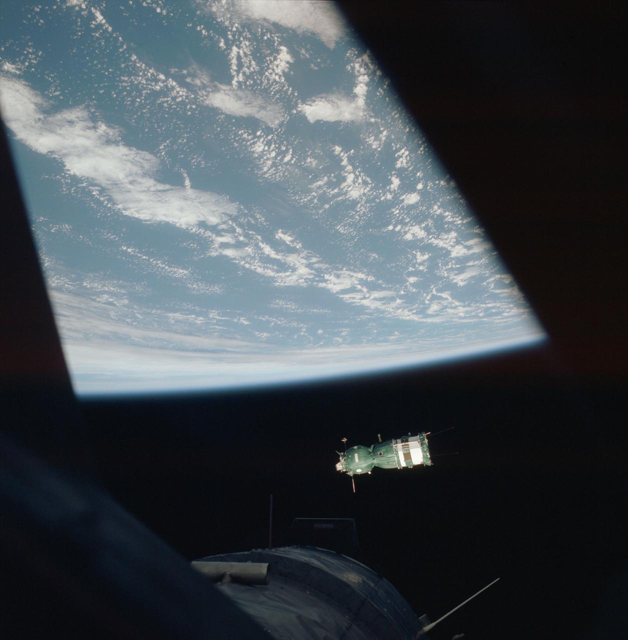 AST-02-093 (18 July 1975) --- This scene photographed with a hand-held 70mm camera from a rendezvous window of the American Apollo spacecraft in Earth orbit shows the Soviet Soyuz spacecraft contrasted against a black-sky background with Earth's horizon below.  The three major components of the Soyuz are the spherical-shaped Orbital Module (OM), the bell-shaped Descent Vehicle (DV) and the cylindrical-shaped instrument Assembly Module (AM). The docking system on the Orbital Module was specially designed to interface with the docking system on the Apollo's Docking Module (DM). The DM is visible very faintly at the bottom of the picture. The ASTP astronauts and cosmonauts visited each other's spacecraft while the Soyuz and Apollo were docked in Earth orbit for two days.