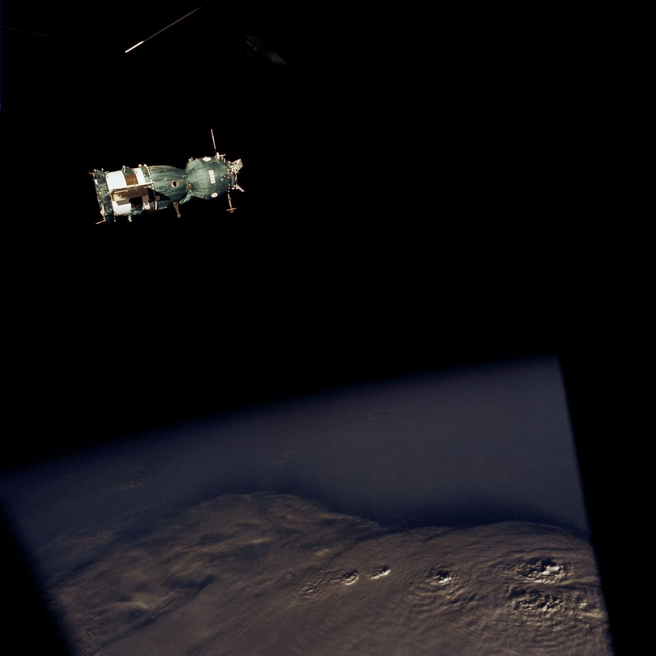 AST-02-096 (18 July 1975) --- This scene photograph from a rendezvous window of the American Apollo spacecraft in Earth orbit shows the Soviet Soyuz spacecraft contrasted against a black-sky background with a heavily cloud-covered Earth below. The three major components of the Soyuz are the spherical-shaped Orbital Module, the bell-shaped Descent Vehicle, the cylindrical-shaped Instrument Assembly Module. The docking system on the Orbital Module was specially designed to interface with the docking system on the Apollo's Docking Module. The ASTP astronauts and cosmonauts visited each other's spacecraft while the Soyuz and Apollo were docked in Earth orbit for two days.
