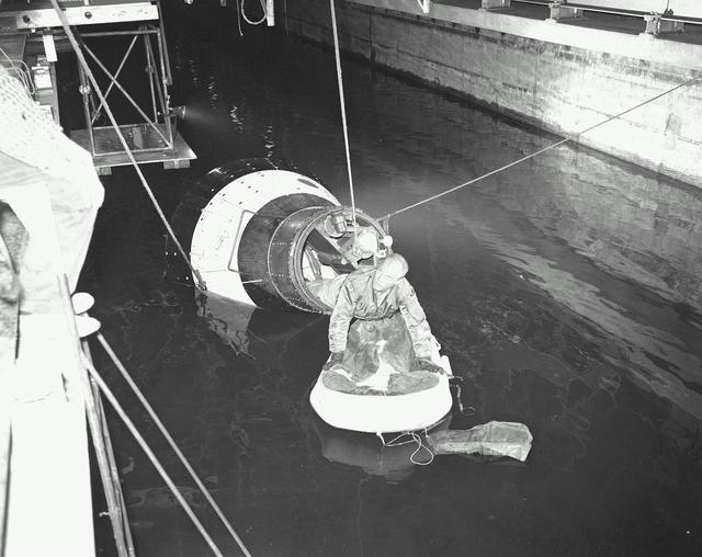 B60-00285 (1960) --- Astronaut John H. Glenn Jr., pilot of the Mercury Atlas 6 spaceflight, emerges from an egress trainer during training activity at the Langley Research Center. He is attempting to transfer onto a life raft from the mock-up of the Mercury capsule. Photo credit: NASA