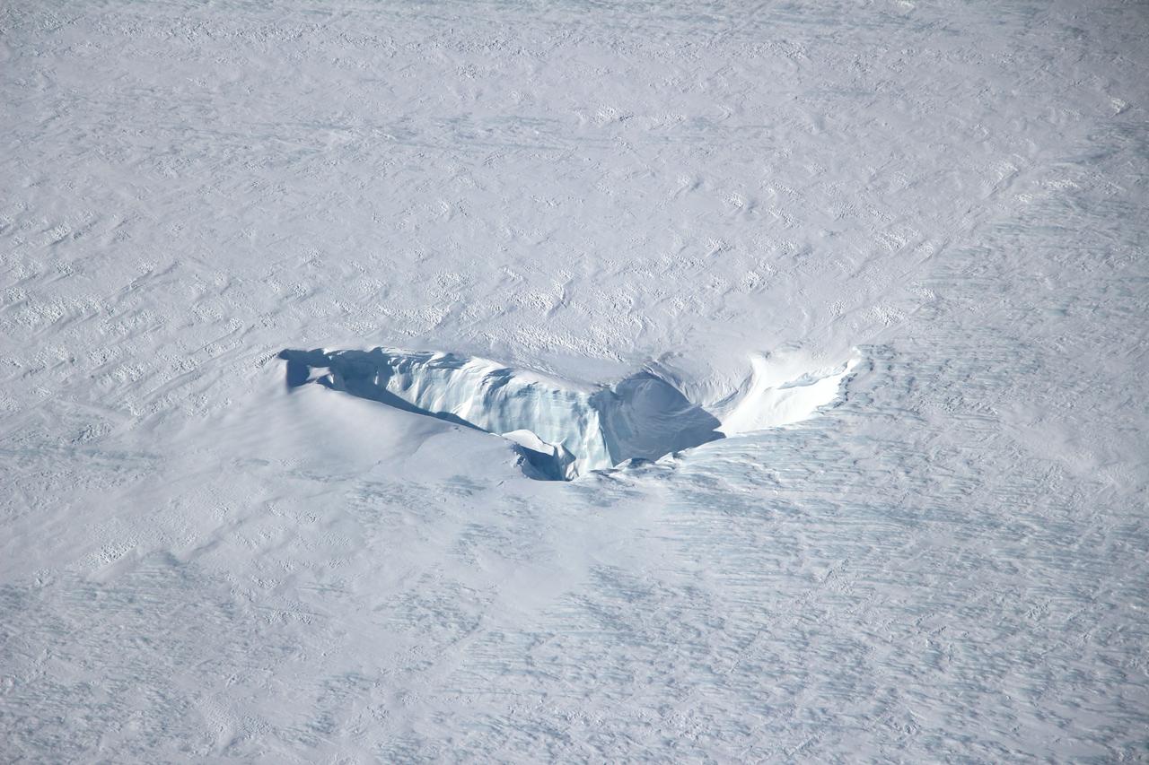 Scientists and crew with NASA’s Operation IceBridge, which makes annual aerial surveys of polar ice, are wrapping up their seventh campaign over the Arctic. In spring 2015, the team began using a different research aircraft—an adapted C-130 Hercules. They also added four new high-priority targets in the rapidly changing region of northeast Greenland.  Many of the flights, however, were routine. And that’s exactly the point; making measurements over the same path each year provides continuity between NASA’s Ice, Cloud, and Land Elevation Satellite (ICESat) missions—the first of which ended in 2009 and the second of which is scheduled for launch in 2017. Repeat measurements show how a landscape changes over time.  One area that has been surveyed repeatedly is northern Greenland’s Ryder Glacier. This photograph, taken during the IceBridge flight on May 6, 2015, shows a large moulin—dozens of meters across—atop this glacier. Moulins are holes in the ice sheet that drain melt water from the ice sheet’s surface to the bottom or out to the sea. Scientists are working to figure out what happens to melt water once it enters a moulin.