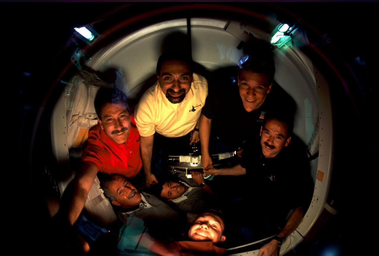 ISS002-311-032 (23 April 2001) --- The six astronauts and one cosmonaut comprising the STS-100 crew assemble in the Pressurized Mating Adapter (PMA-2) while waiting to visit the Expedition Two crew and the International Space Station (ISS). With his arm extended to left foreground is astronaut Kent V. Rominger, STS-100 mission commander.  In the circular arrangement of crewmembers, clockwise from Rominger's position, are astronauts Umberto Guidoni, Scott E. Parazynski, Chris A. Hadfield, Jeffrey S. Ashby and John L. Phillips. Cosmonaut Yuri V. Lonchakov's head emerges at bottom center. On the other side of the glass were the Expedition Two crewmembers--cosmonaut Yury V. Usachev and astronauts James S. Voss and Susan J. Helms. Lonchakov and Usachev represent Rosaviakosmos; Hadfield is with the Canadian Space Agency (CSA) and Guidoni is associated with the European Space Agency (ESA). The ten were beginning a day that went on to see the first opening of hatches linking the two spacecraft, an impressive first step by the station's new Canadarm2 and the berthing to the station of Raffaello, the Italian-built logistics module. Hatch opening was set for 4 a.m. (CDT), April 23.