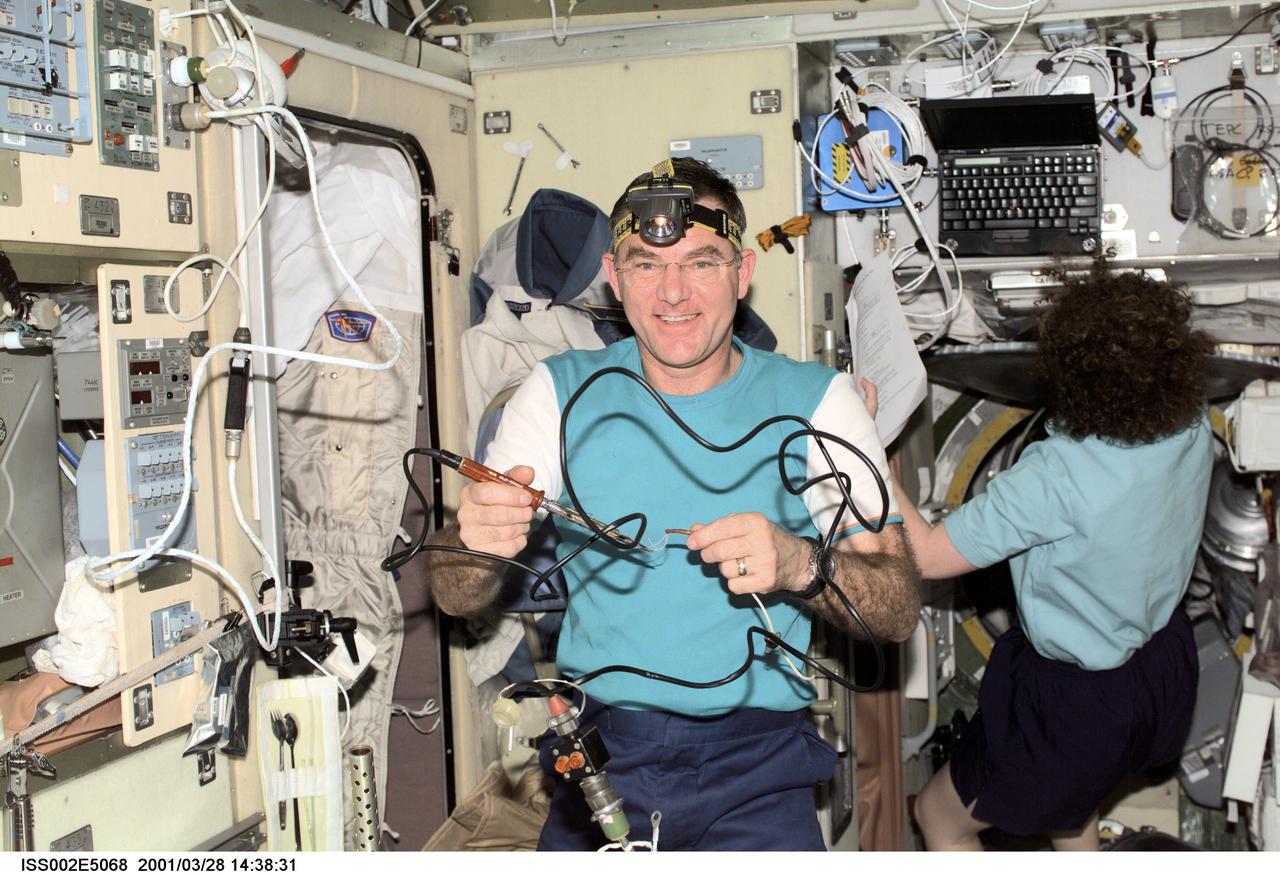 ISS002-E-5068 (28 March 2001) --- Astronaut James S. Voss, Expedition Two flight engineer, prepares to use a soldering tool for a maintenance task  in the Zvezda Service Module onboard the  International Space Station (ISS). Astronaut Susan J. Helms, flight engineer, is in the background.  The image was recorded with a digital still camera.