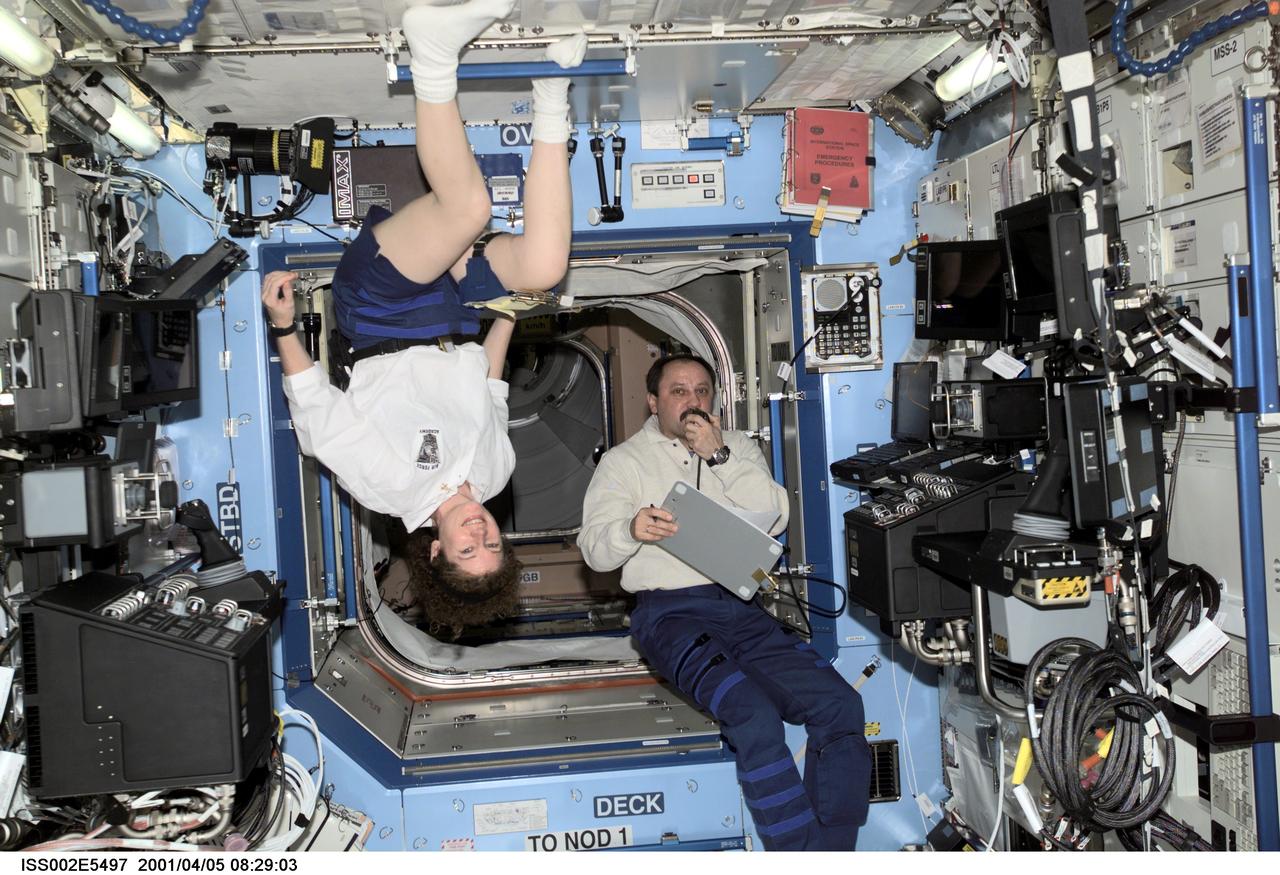 ISS002-E-5497 (05 April 2001) --- Astronaut Susan J. Helms (left), Expedition Two flight engineer, pauses from her work to pose for a photograph while Expedition Two mission commander, cosmonaut Yury V. Usachev, speaks into a microphone aboard the U.S. Laboratory / Destiny module of the International Space Station (ISS). This image was recorded with a digital still camera.