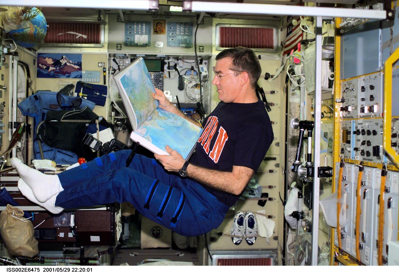 ISS002-E-6475 (29 May 2001) --- James S. Voss, Expedition Two flight engineer, looks over an atlas in the Zvezda Service Module.  The image was taken with a digital still camera.
