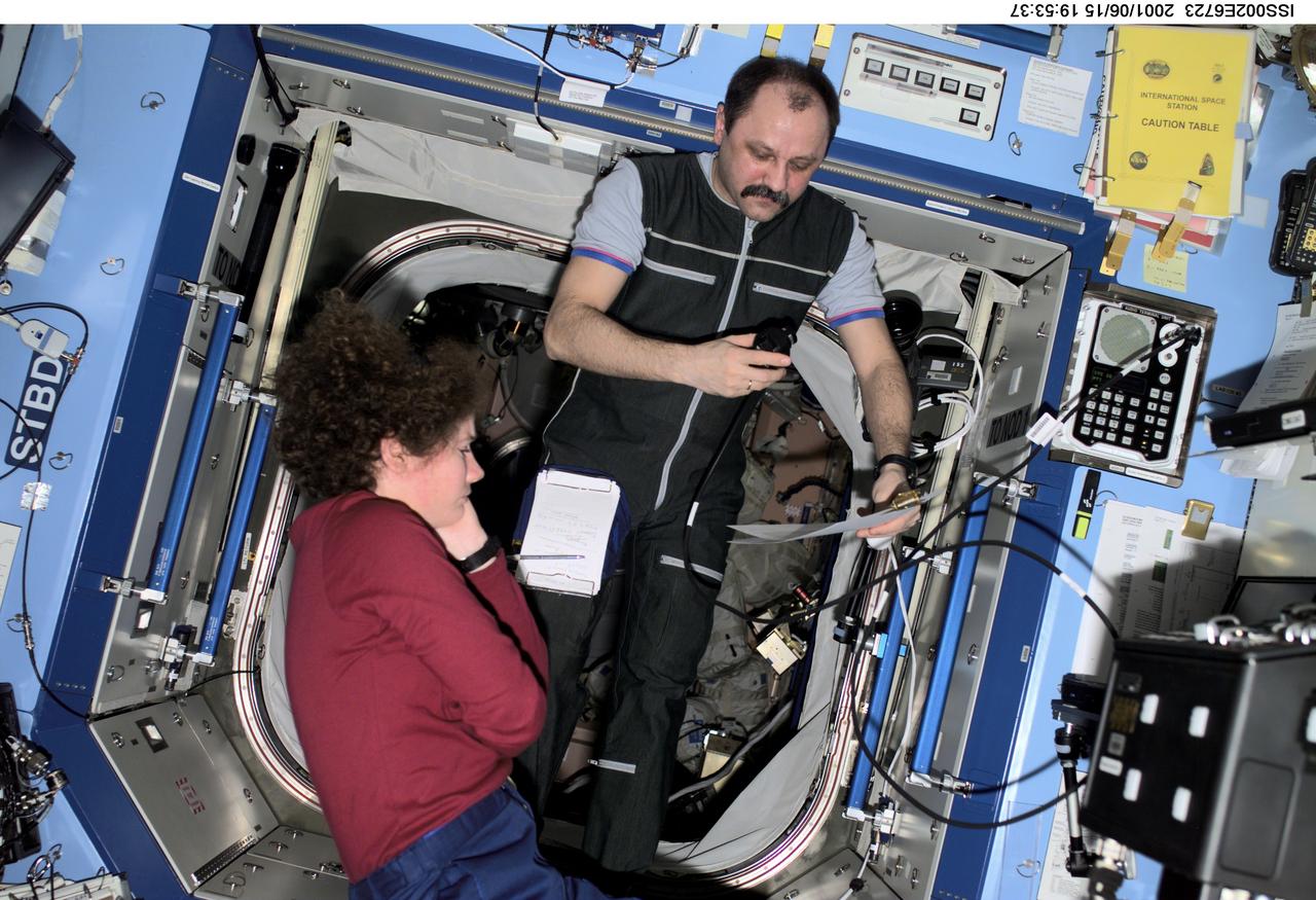 ISS002-E-6723 (15 June 2001) --- Astronaut Susan J. Helms, Expedition Two flight engineer, and cosmonaut Yury V. Usachev, mission commander, discuss a checklist in the Destiny/U.S. Laboratory. Usachev is with Rosaviakosmos. The photo was taken with a digital still camera.