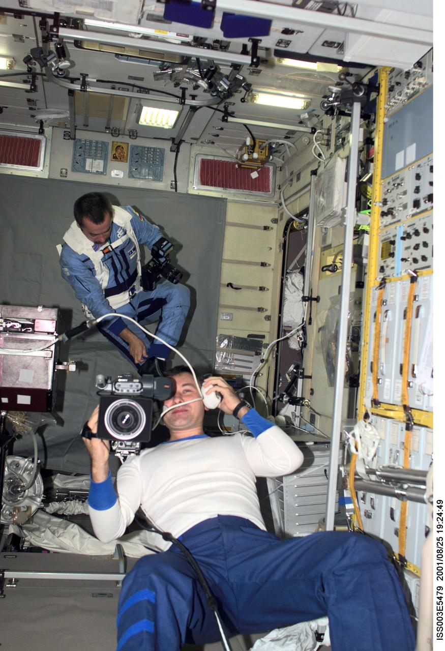 ISS003-E-5479 (24 August 2001) --- Cosmonaut Vladimir Dezhurov, Expedition Three flight engineer, operates a video camera in the Zvezda Service Module.  In the background, cosmonaut Mikhail Tyurin, flight engineer, is visible with a photographic camera.  Tyurin and Dezhurov represent Rosaviakosmos.
