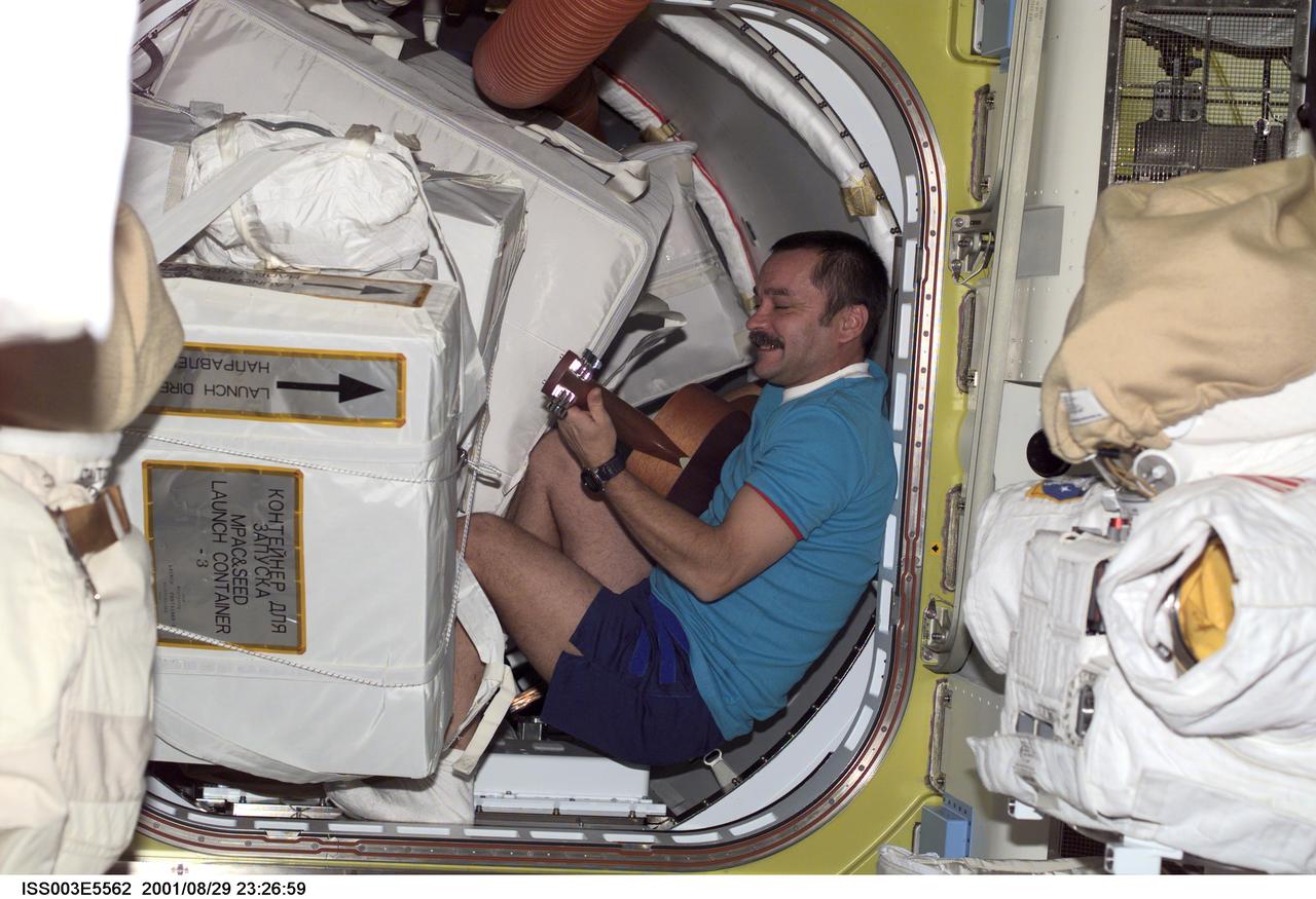 ISS003-E-5562 (29 August 2001) --- Cosmonaut Mikhail Tyurin of Rosaviakosmos, Expedition Three flight engineer, plays a guitar among stowage bags in the hatch area of the Quest Airlock.