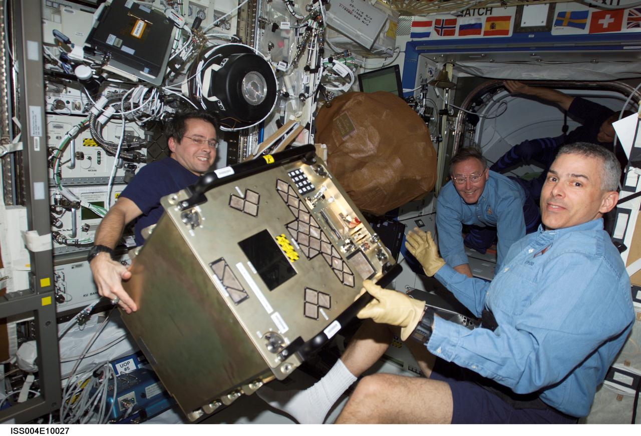 ISS004-E-10027 (12 April 2002) --- Astronauts Daniel W. Bursch (left), Expedition Four flight engineer, and Lee M. E. Morin, STS-110 mission specialist, move equipment in the Destiny laboratory on the International Space Station (ISS). Astronaut Jerry L. Ross, STS-110 mission specialist, is visible in the background.