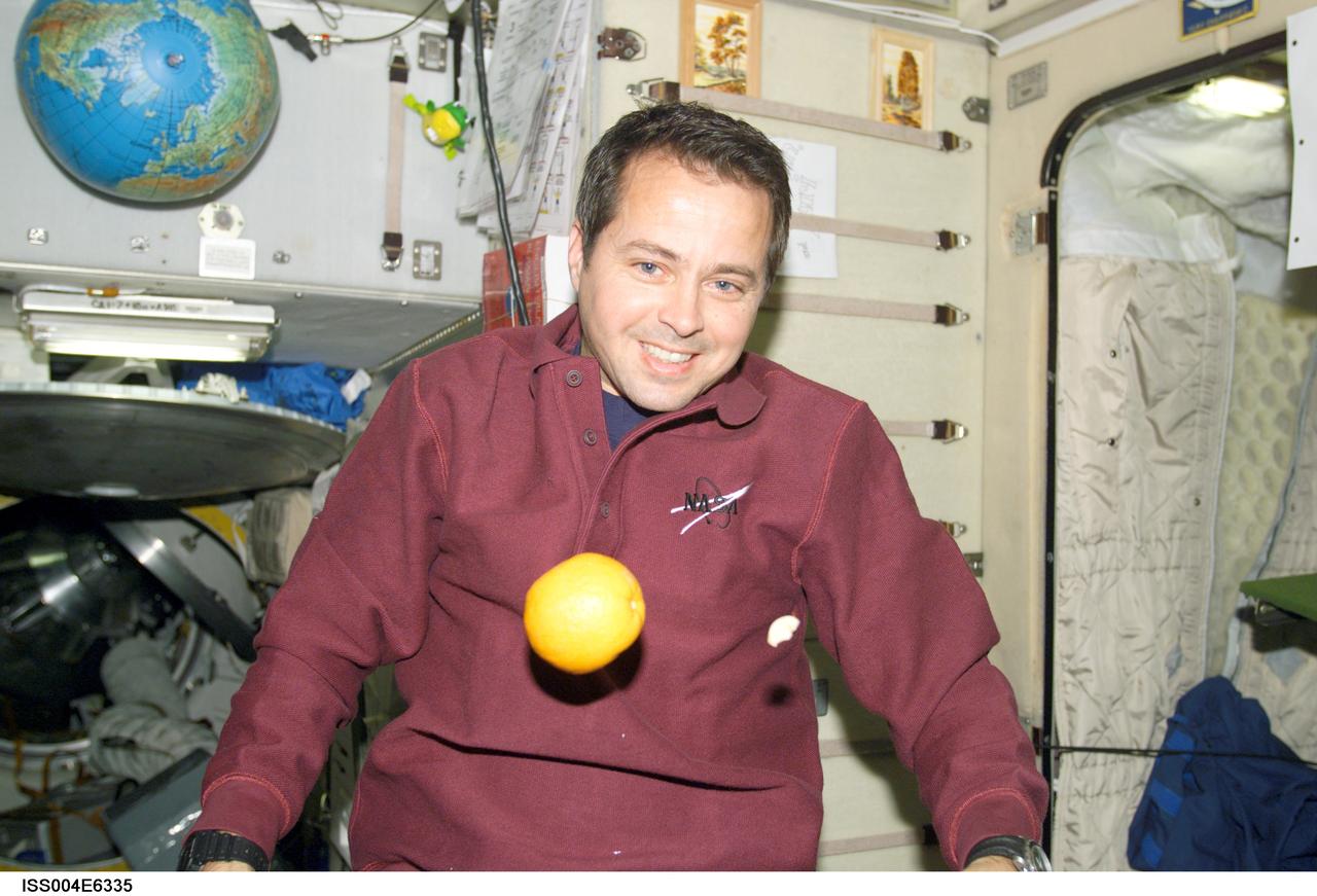 ISS004-E-6335 (January 2002) --- Astronaut Daniel W. Bursch, Expedition Four flight engineer, is photographed in the Zvezda Service Module on the International Space Station (ISS).  An orange floats freely in front of Bursch. The image was taken with a digital still camera.