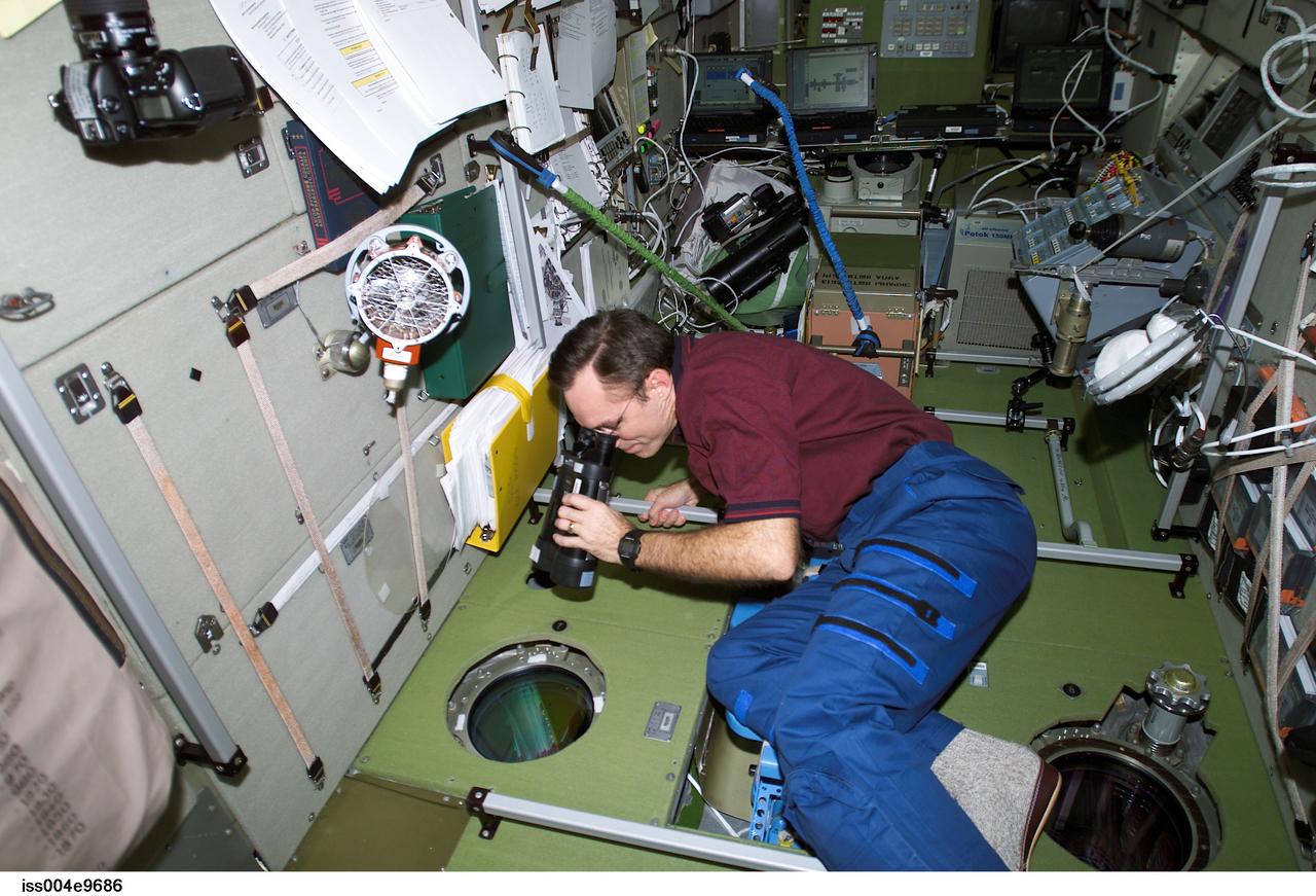 ISS004-E-9686 (24 March 2002) --- Astronaut Carl E. Walz, Expedition Four flight engineer, uses binoculars to look out a window in the Zvezda Service Module on the International Space Station (ISS). The crew anticipated the approach of a Progress supply vehicle about the time this image was taken.