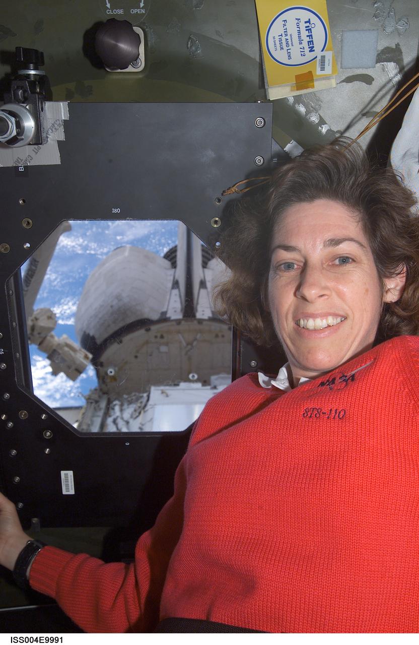ISS004-E-9991 (10 April 2002) --- Astronaut Ellen Ochoa, STS-110 mission specialist, is photographed near a Destiny laboratory window on the International Space Station (ISS). Portions of the Space Shuttle Atlantis and the Canadarm2 are visible through the window.