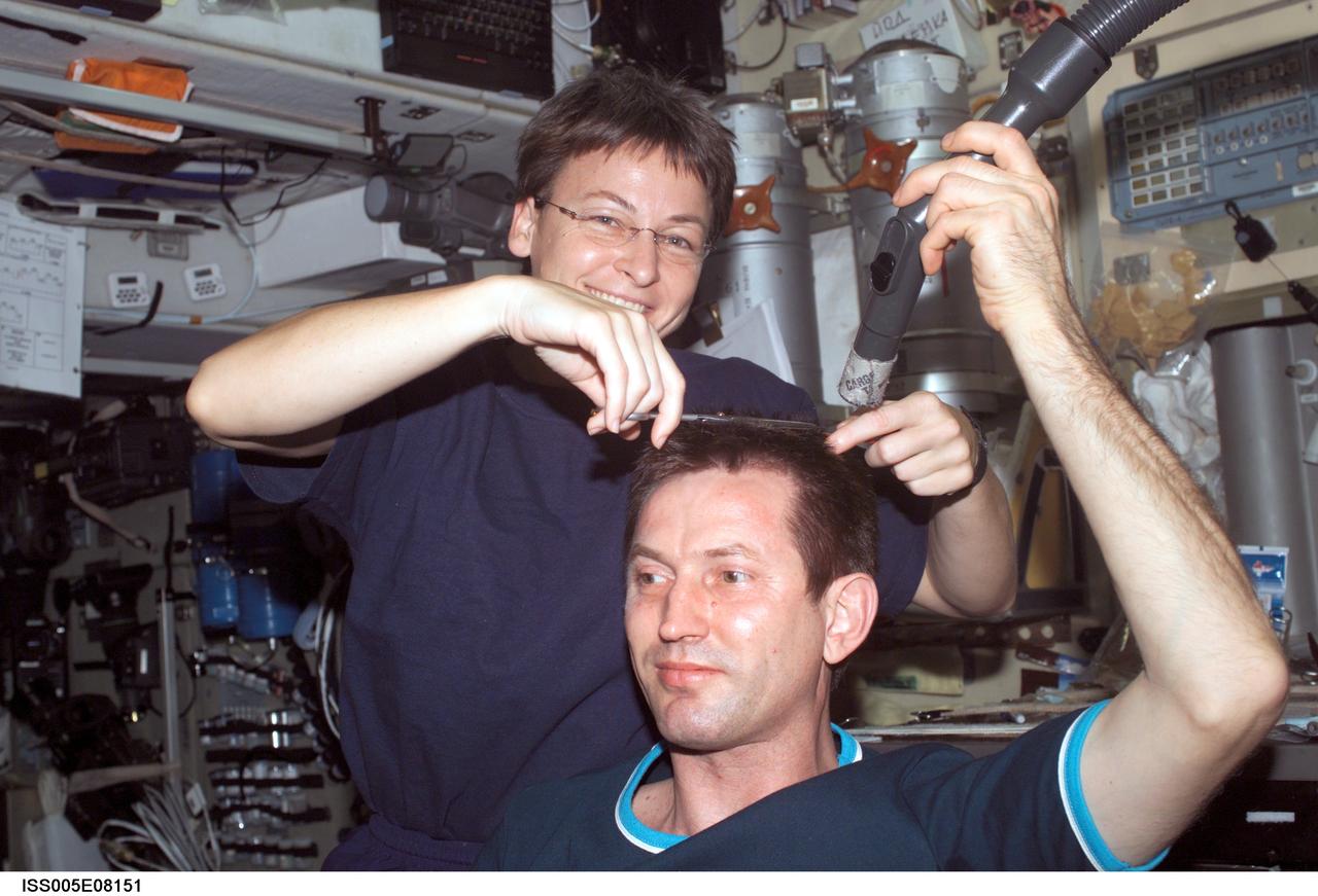 ISS005-E-08151 (July 2002) --- Astronaut Peggy A. Whitson, Expedition Five flight engineer, cuts cosmonaut Sergei Y. Treschev&#0146;s hair in the Zvezda Service Module on the International Space Station (ISS). Treschev, flight engineer representing Rosaviakosmos, holds a vacuum device the crew has fashioned to garner freshly cut hair, which is floating freely.