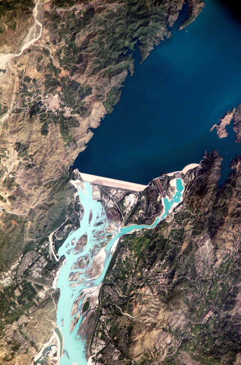 ISS005-E-12804 (6 September 2002) --- Tarbela Dam, Pakistan is featured in this image photographed by an Expedition 5 crewmember on the International Space Station (ISS). The Indus River basin extends from the Himalaya mountain ranges forming the northeastern boundary of Pakistan, to the alluvial plains of Sindh near the Arabian Sea coastline. Tarbela Dam is part of the Indus Basin Project that resulted from a water treaty signed in 1960 between India and Pakistan. This treaty guaranteed Pakistan water supplies independent of upstream control by India. Designed primarily for water storage rather than power generation, the dam was completed in 1977. Turquoise waters of the Indus River (to the south of the dam) reflect the high proportion of silt and clay suspended in waters released by the spillways (chutes on either of side of the main dam). With a volume of 142,000,000 cubic meters, the Tarbela Dam is the largest earth and rockfill dam in the world and stands 147 meters above the Indus riverbed. Its reservoir occupies an area of 37 square kilometers. While the dam has fulfilled its purpose in storing water for agricultural use in Pakistan, there have been environmental consequences to the Indus river delta, according to NASA scientists who are studying the Space Station photography. Reduction of seasonal flooding and reduced water flows to the delta have resulted in decrease of mangrove stands and abundance of some fish species.